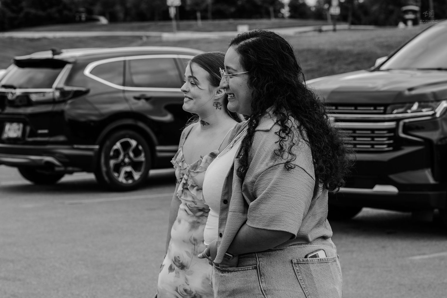 Two smiling women walk side by side in a parking lot in this black and white candid photo.