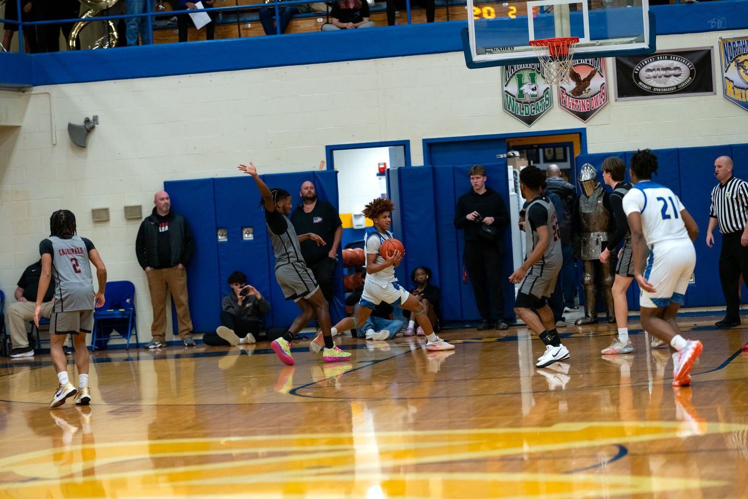 Players compete near the basket during an intense indoor high school basketball game with spectators watching.