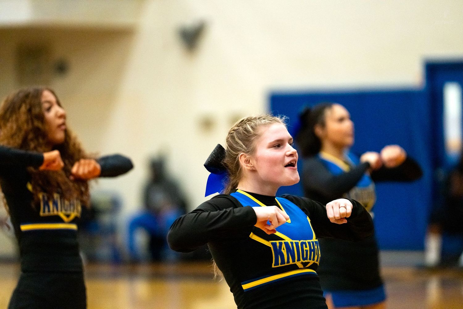 Knights cheerleaders in black and blue uniforms perform synchronized routine at basketball game.