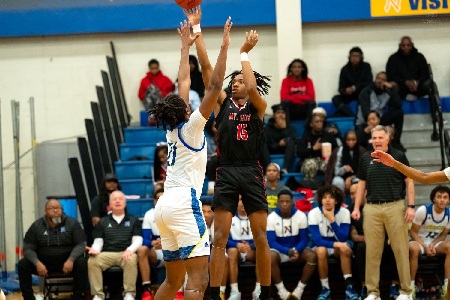 Player #15 in black uniform shoots over defender during high school basketball game.