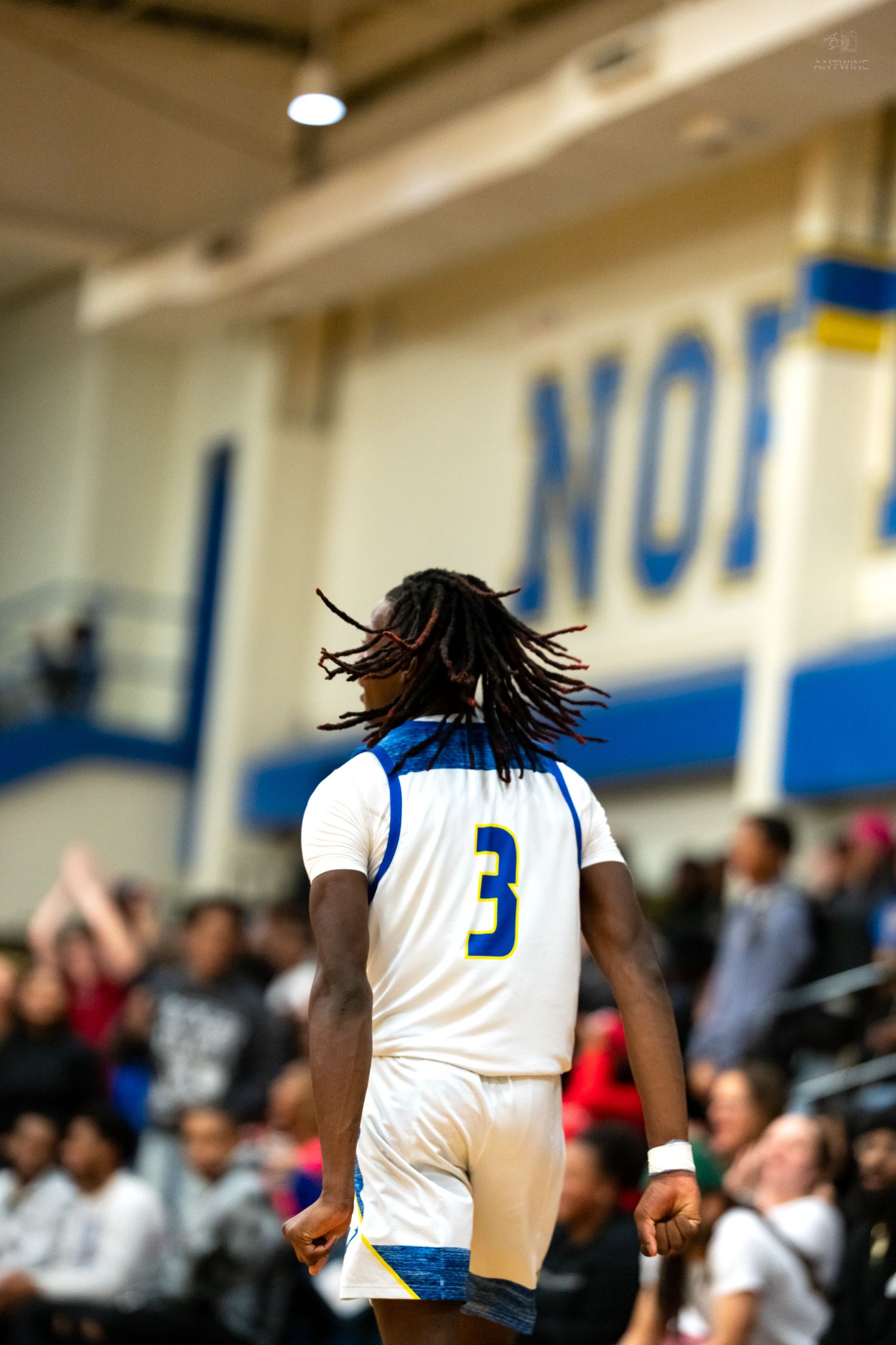 High school basketball player number 3 with dreadlocks walks on court before an energetic crowd.