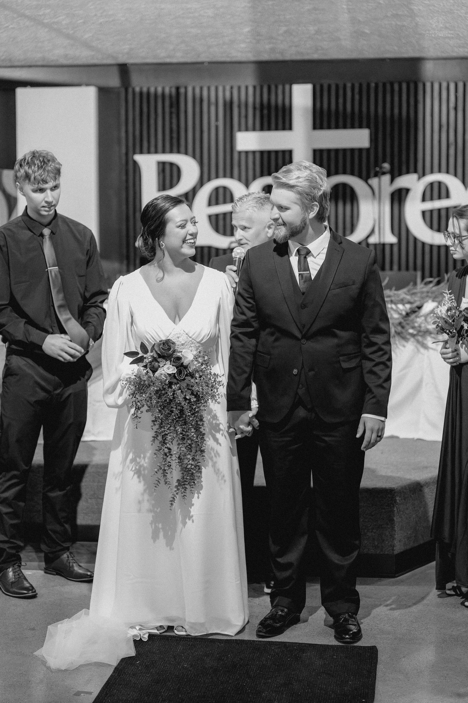 Newlyweds smile joyfully as they walk down the aisle after their wedding ceremony in black and white.
