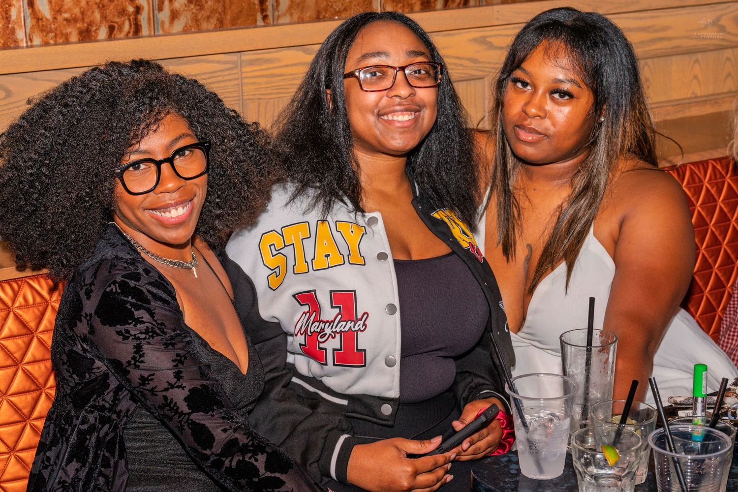 Three women posing together smiling at a nightclub booth.