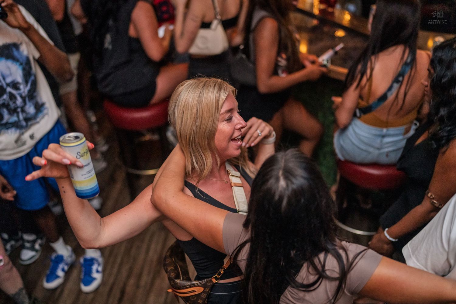 Woman holding a canned drink laughing and dancing with friends at a crowded bar.