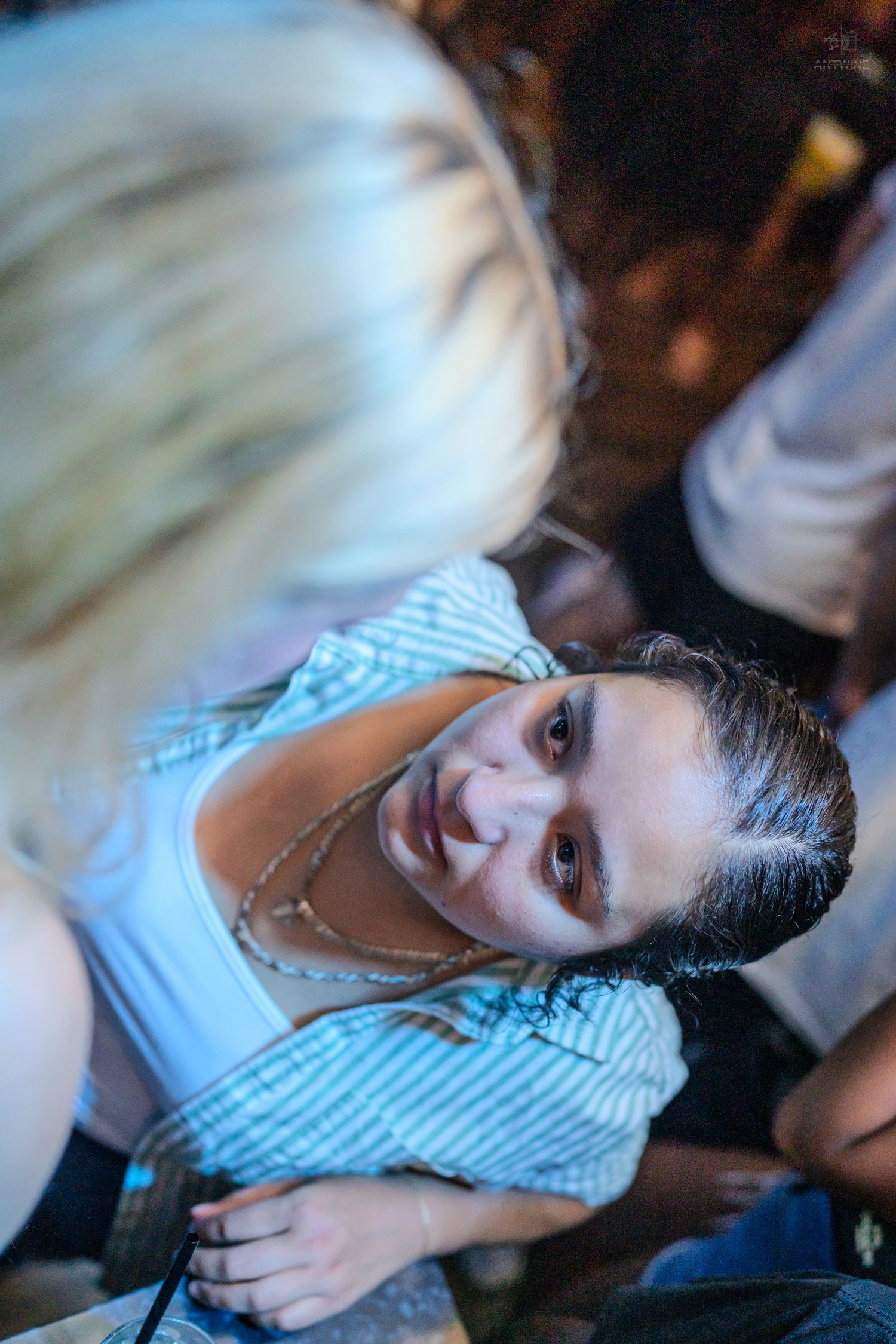 Happy young woman with layered necklaces smiling up at camera in a crowded nightclub.