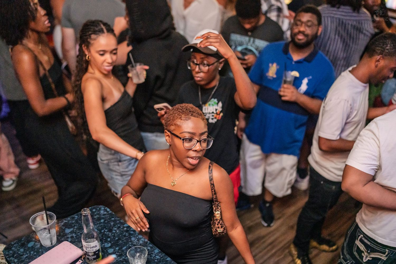 Woman in black dress enjoys a crowded nightclub party with friends dancing nearby.