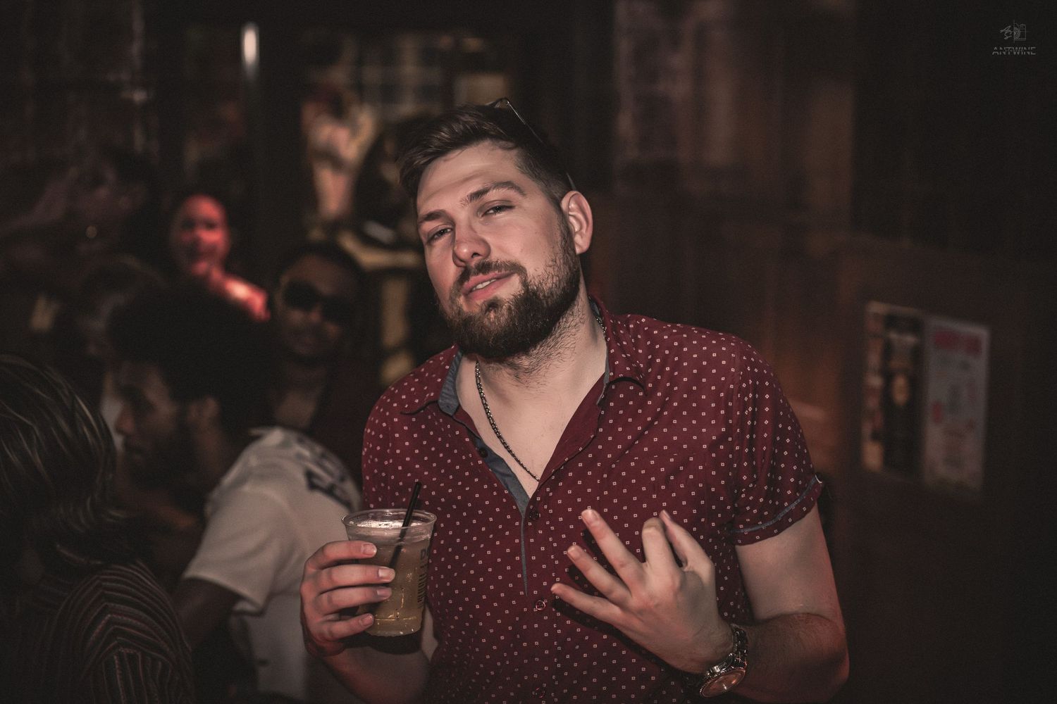Bearded man holding a drink and smiling at a dimly lit bar.
