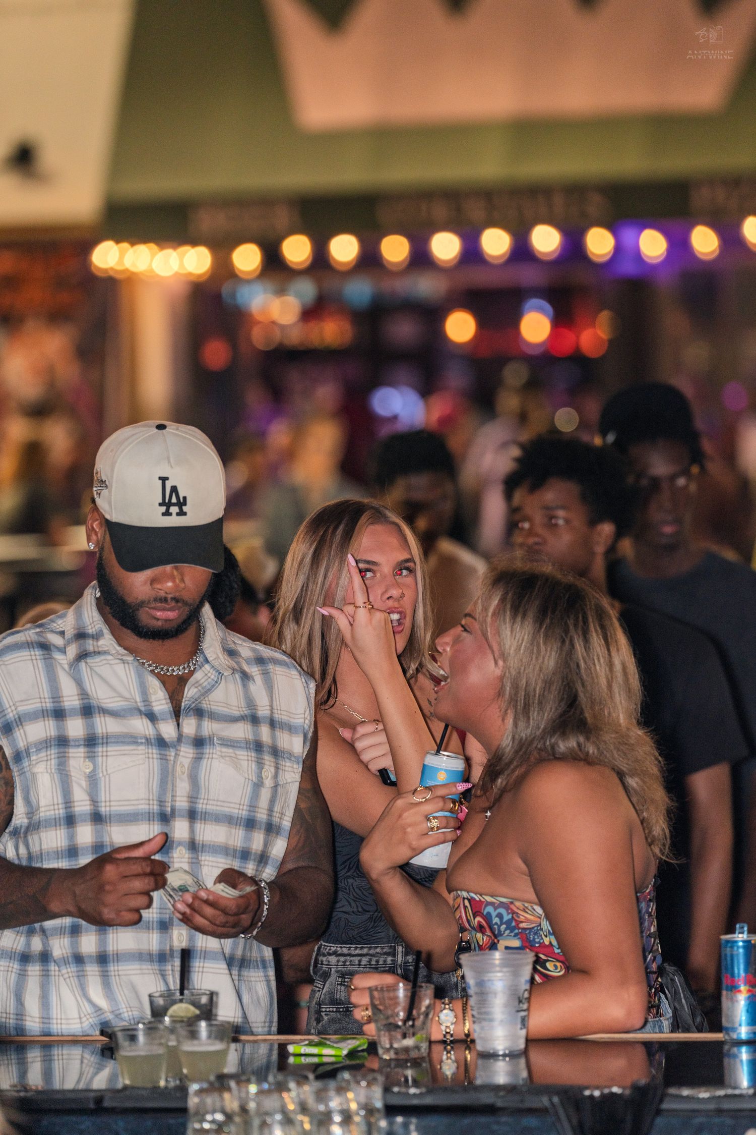 Group of friends socializing at a bar counter with colorful bokeh lights in background.