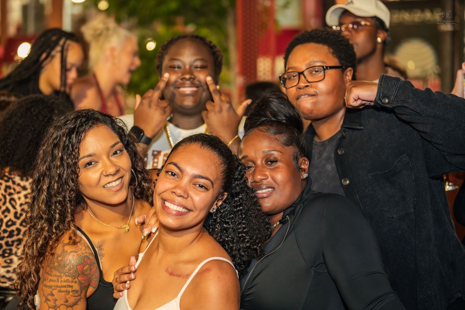 Group of smiling friends posing together for a photo at an outdoor nighttime social gathering.