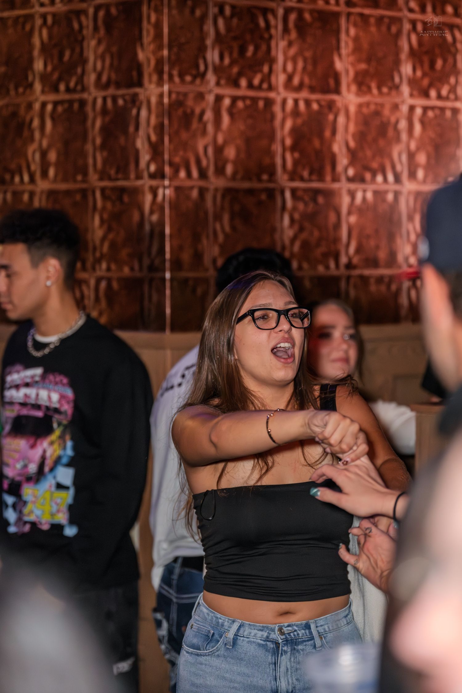 Young woman in black crop top and glasses dancing energetically at a nightclub.