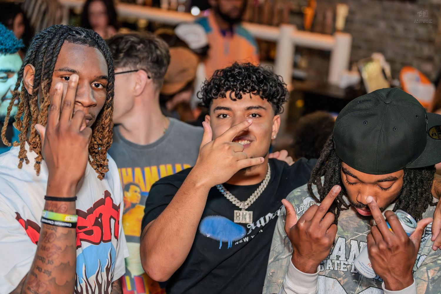 Three young men posing together at a lively bar or nightclub event.