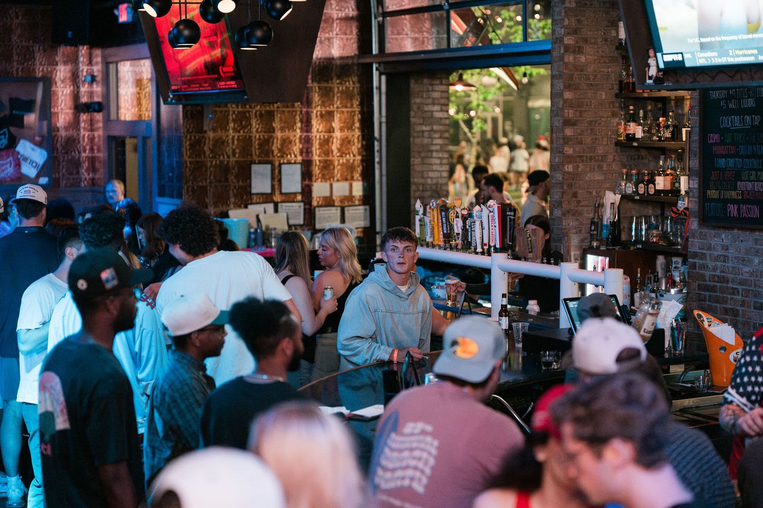 Busy bar with patrons gathered around counter, bartenders serving drinks in a vibrant rustic nightlife venue.