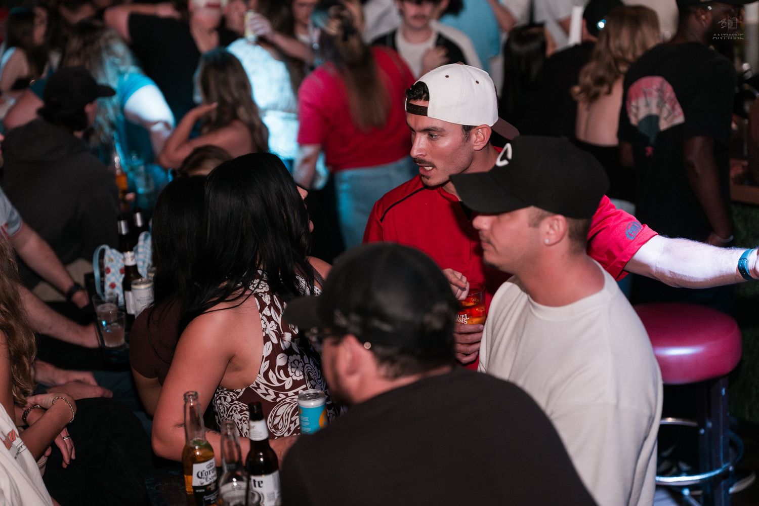 Crowd of people socializing at a lively nightclub bar with bottles and colorful lighting.