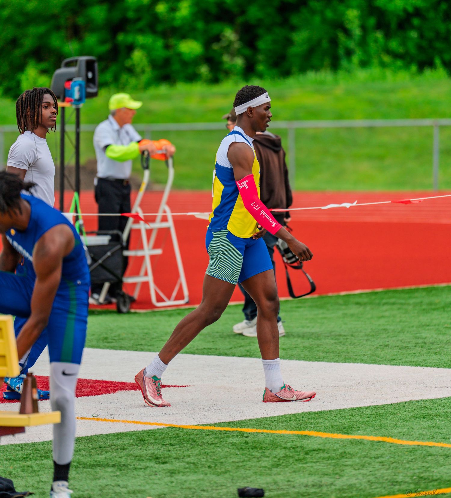 Male athlete in blue and yellow Knights uniform walks along red track at field event.