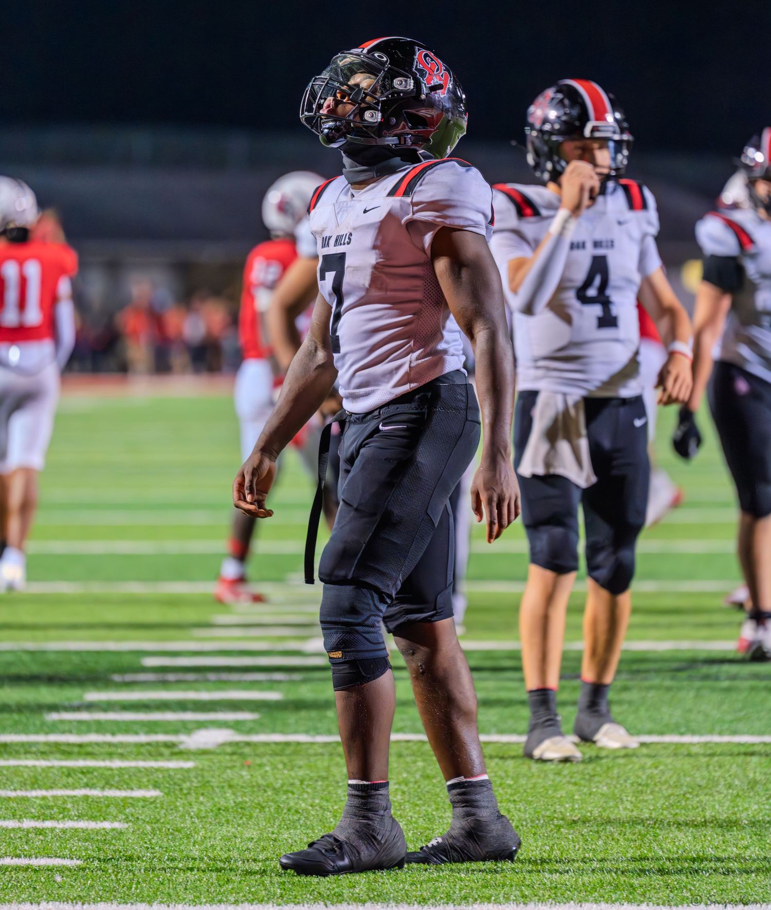 Football player #7 in dark uniform looks skyward on the field during a night game.