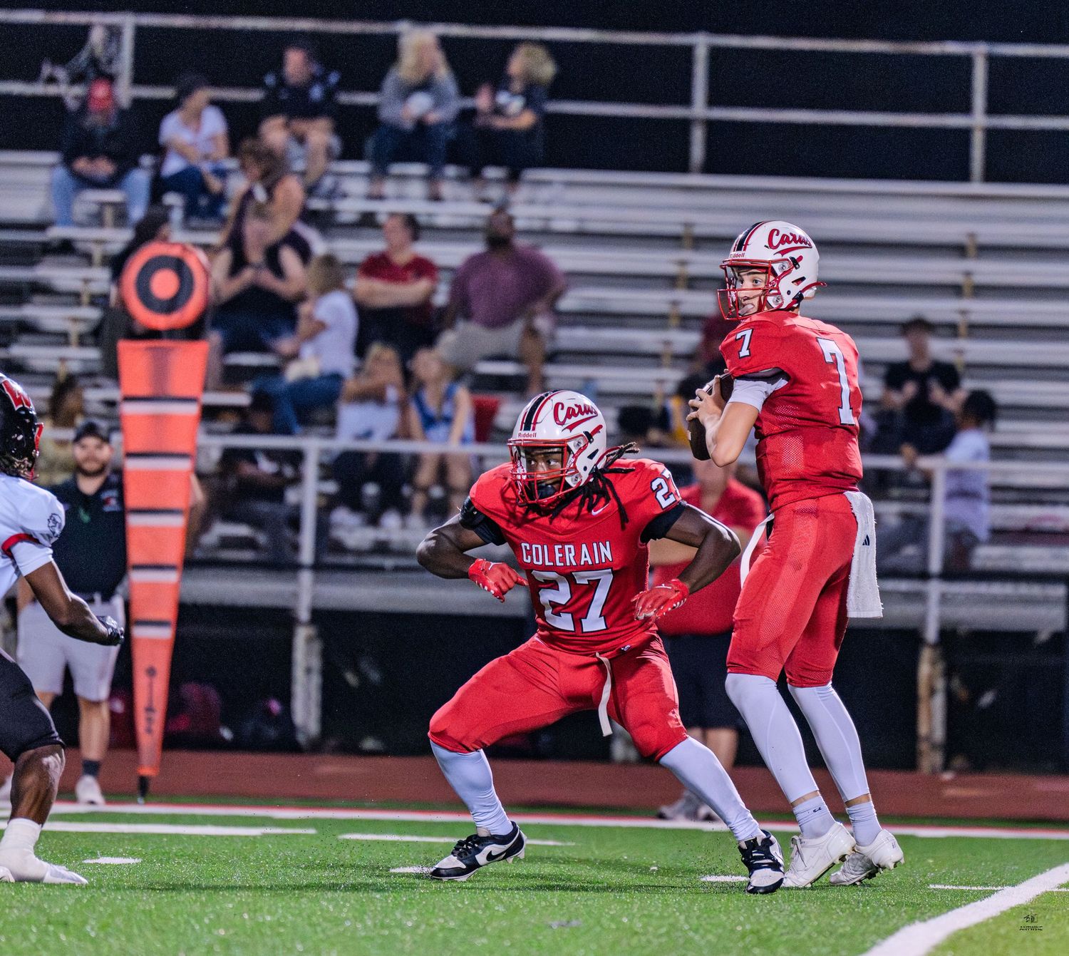 Colerain Cardinals #27 blocks for quarterback #7 during a high school football game.