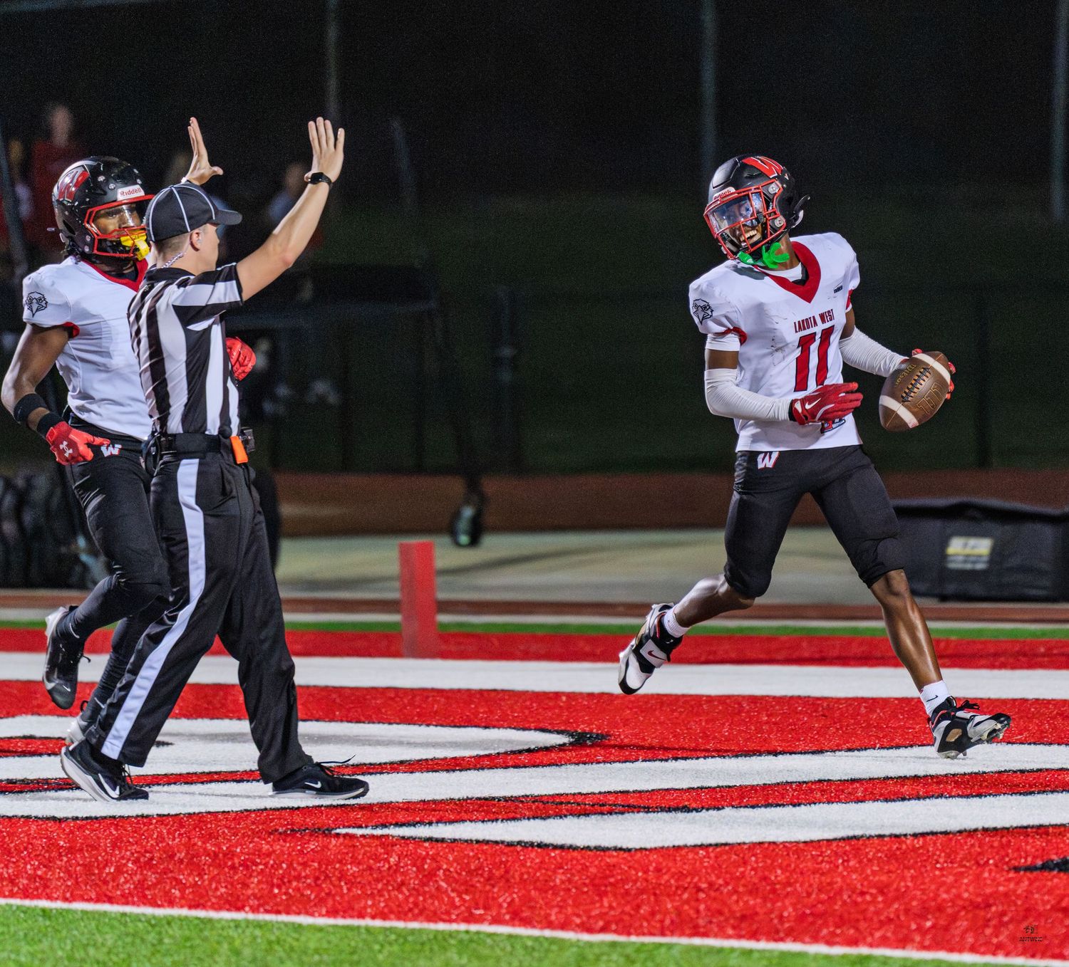 Player number 11 celebrates touchdown in end zone as referee signals score during high school football game.