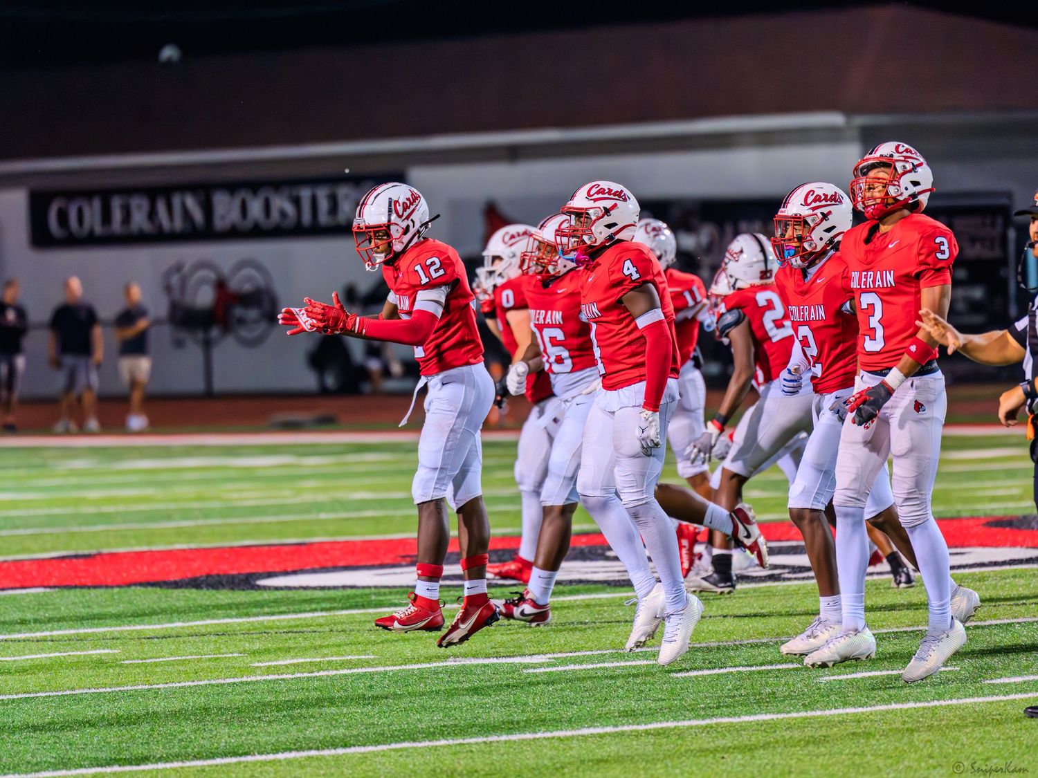 Colerain football players in red celebrate on the field in front of the Colerain Boosters sign.