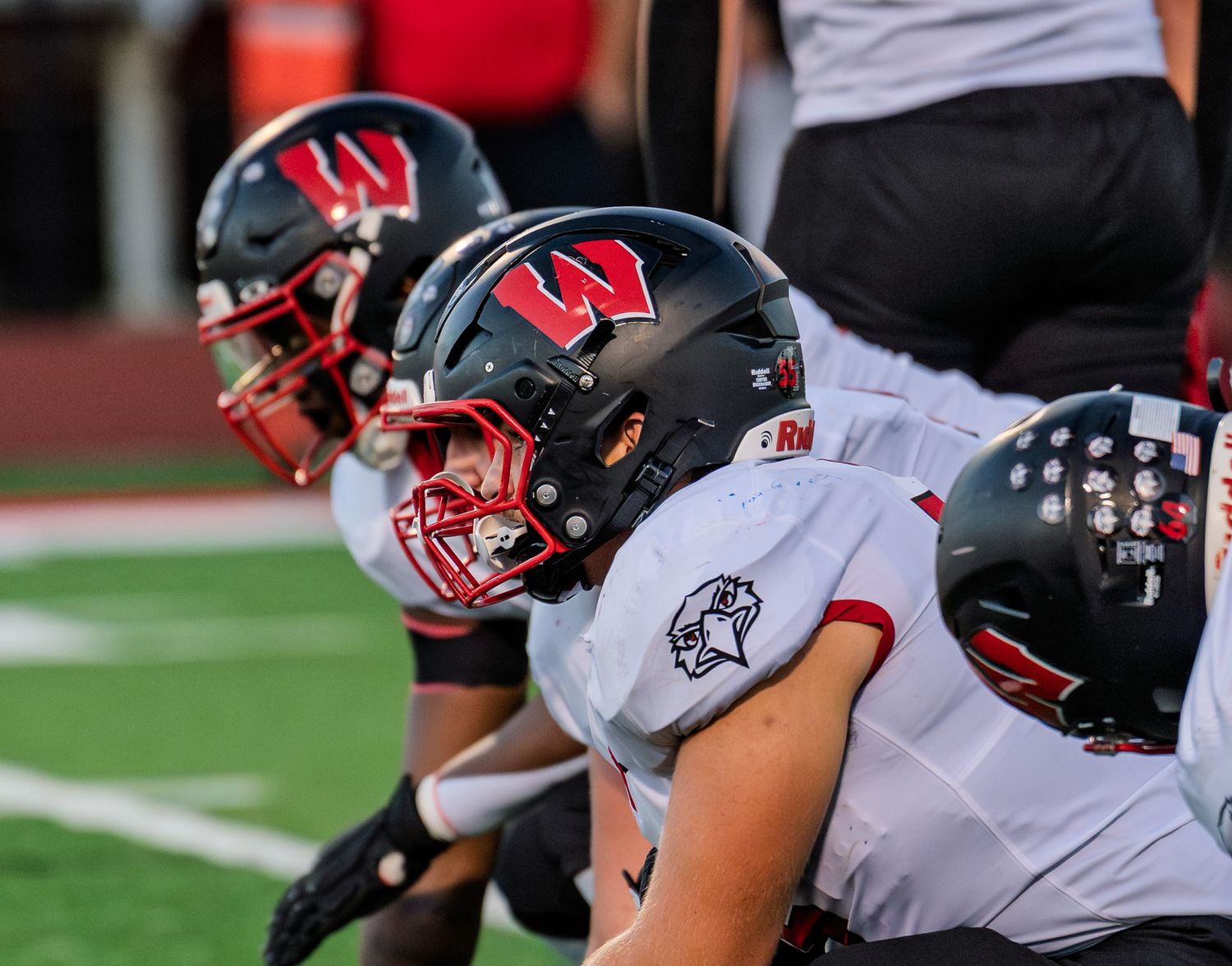 Football players in black and white uniforms line up at scrimmage during a night game.