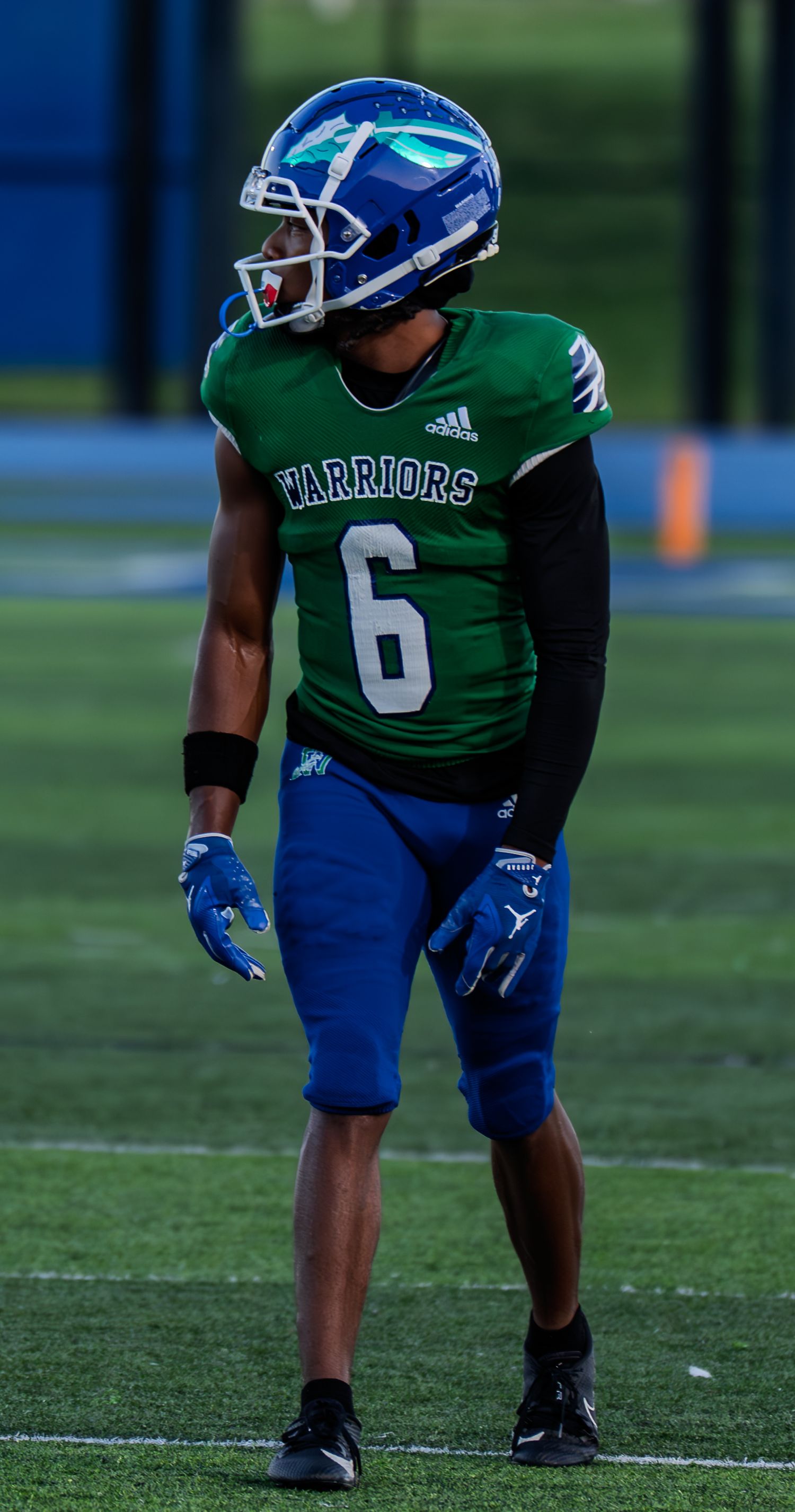 Warriors football player number 6 in green and blue Adidas uniform stands on the field during a night game.