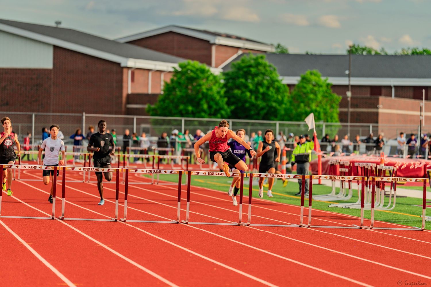 Male athletes leap over hurdles simultaneously during a competitive high school track and field event.