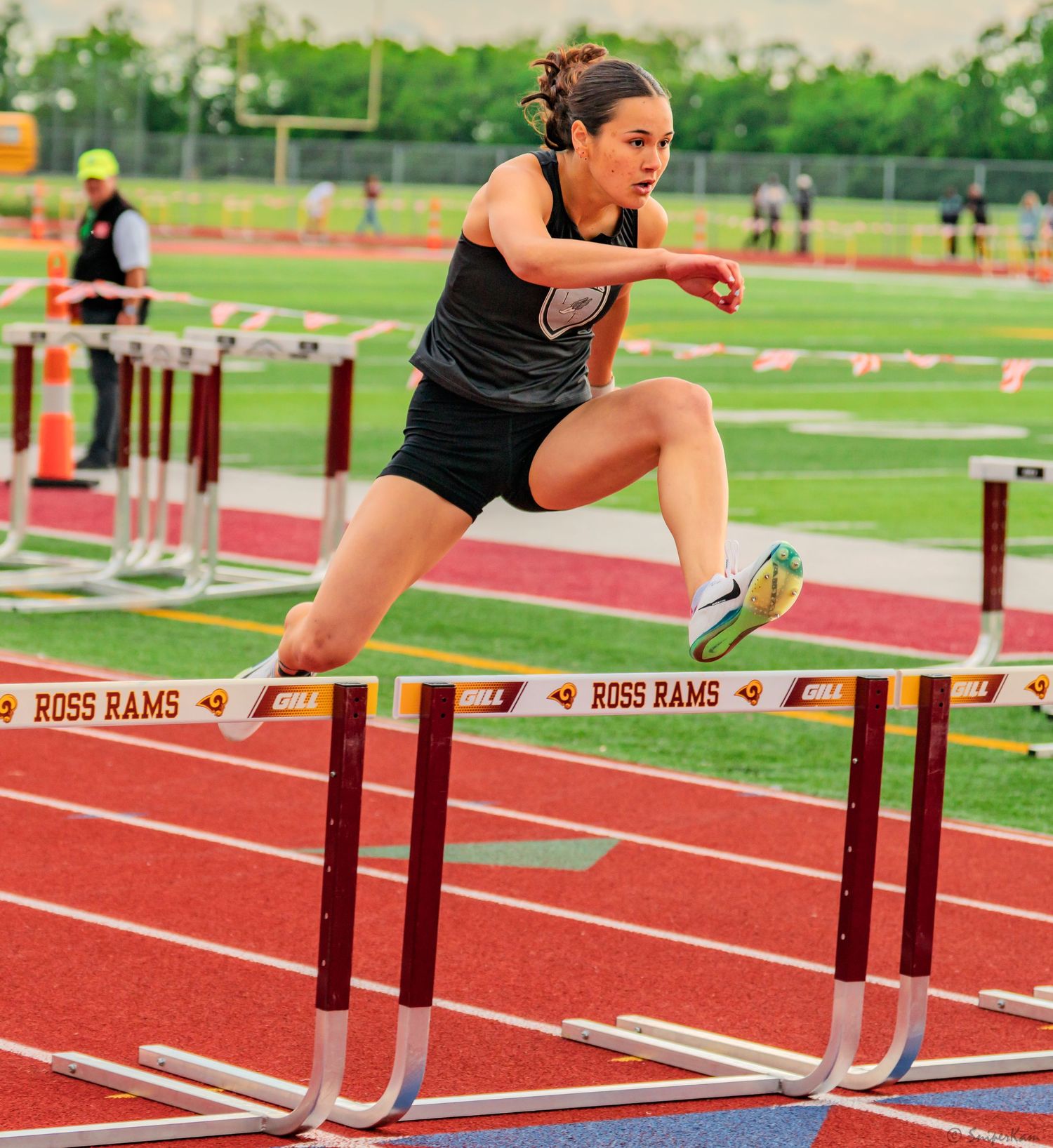 Female athlete clears a hurdle during a track meet at Ross Rams stadium.