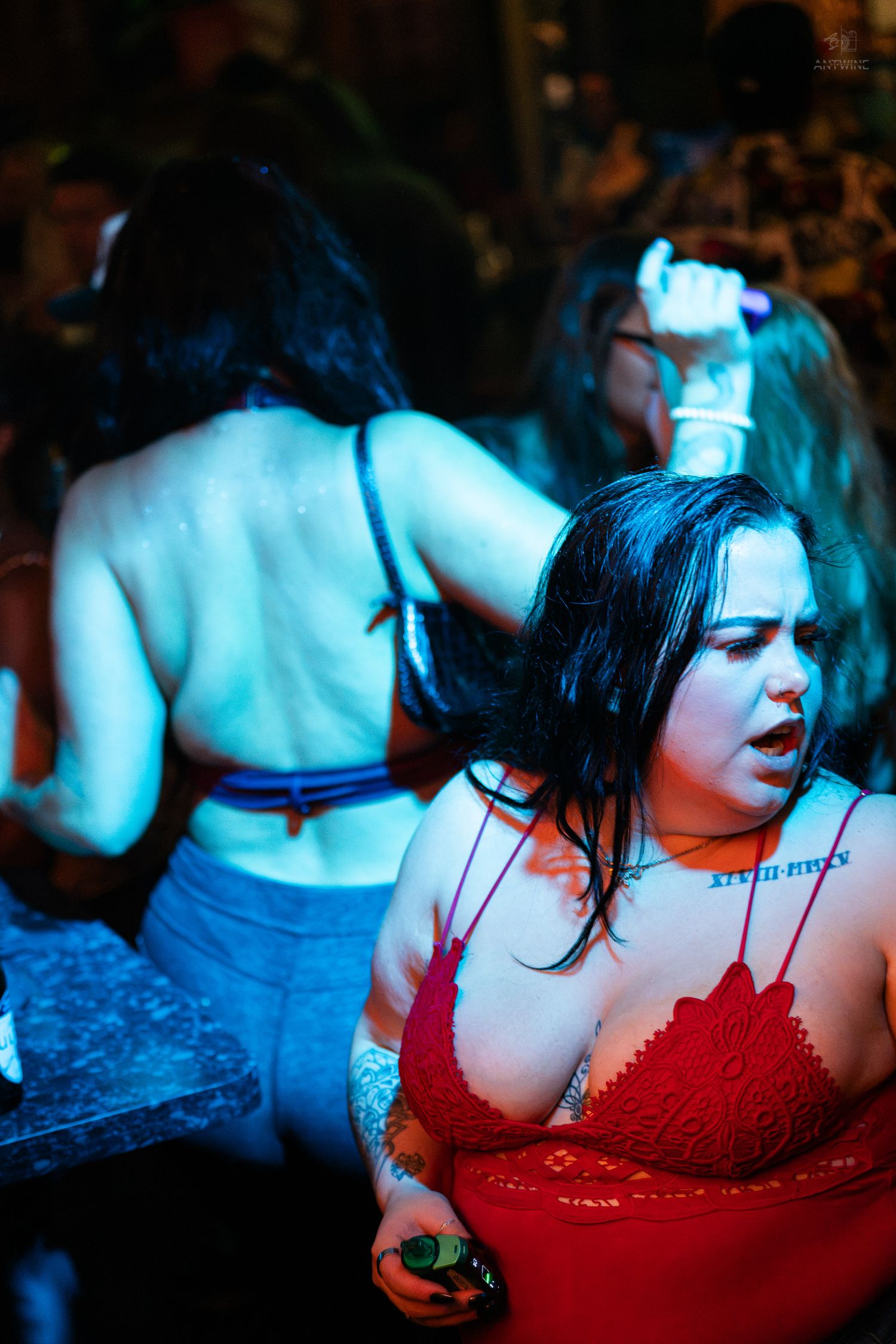 Woman in red lace top dancing under blue lights at a crowded nightclub event.