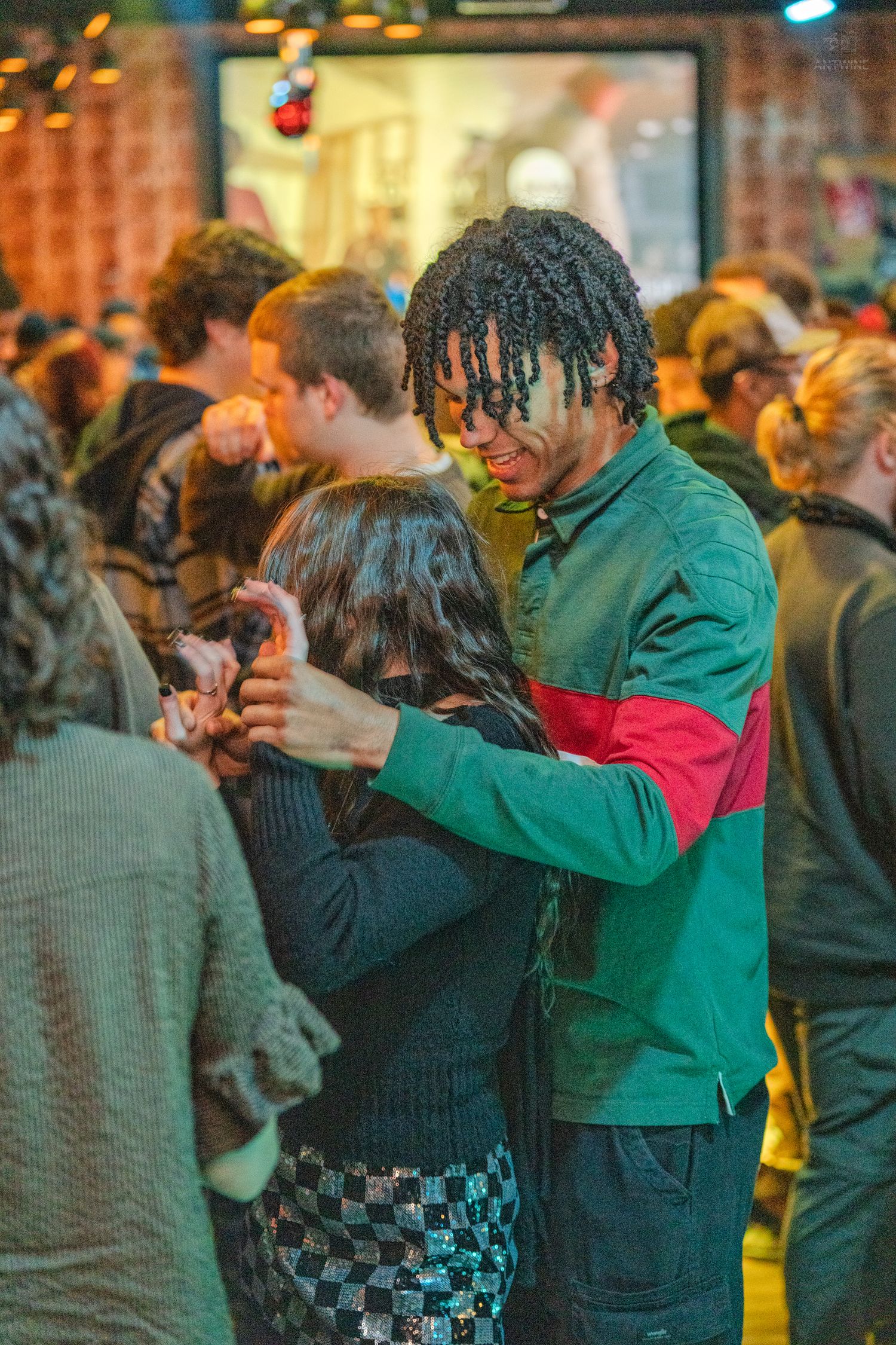 Couple slow dancing closely together in a green jacket at a busy social gathering.