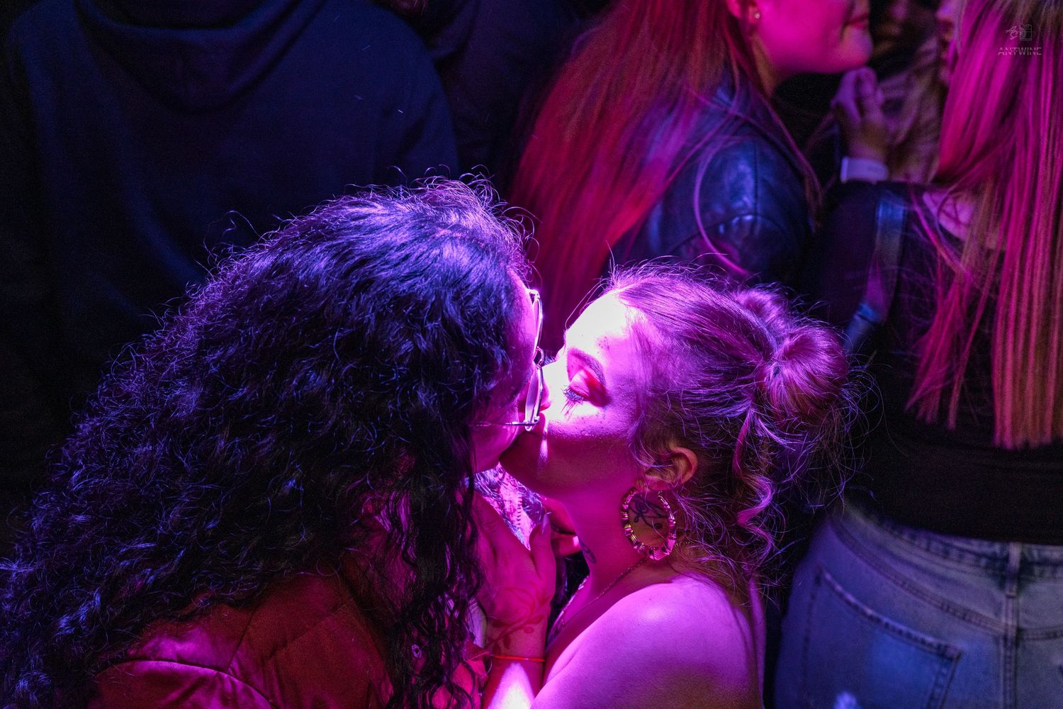 Two women kissing under vibrant pink and purple nightclub lights.