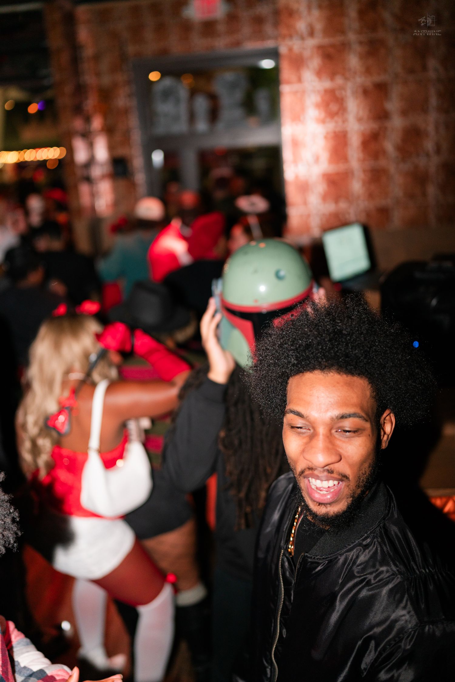 Man with afro smiles at Halloween party with Boba Fett costume visible in background.