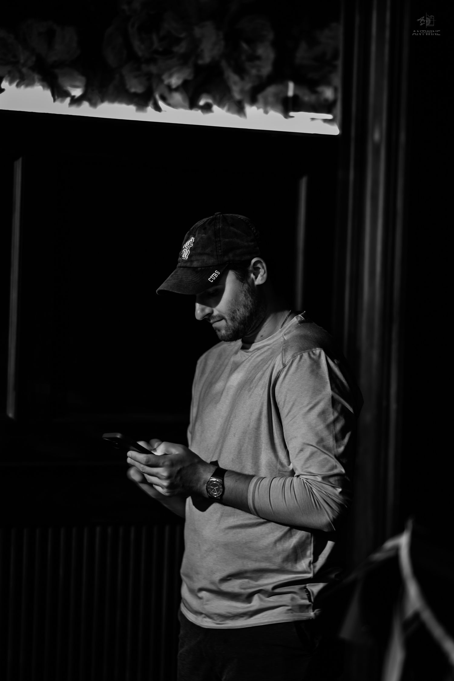 Black and white portrait of a man in a cap looking at his phone in a dark venue.