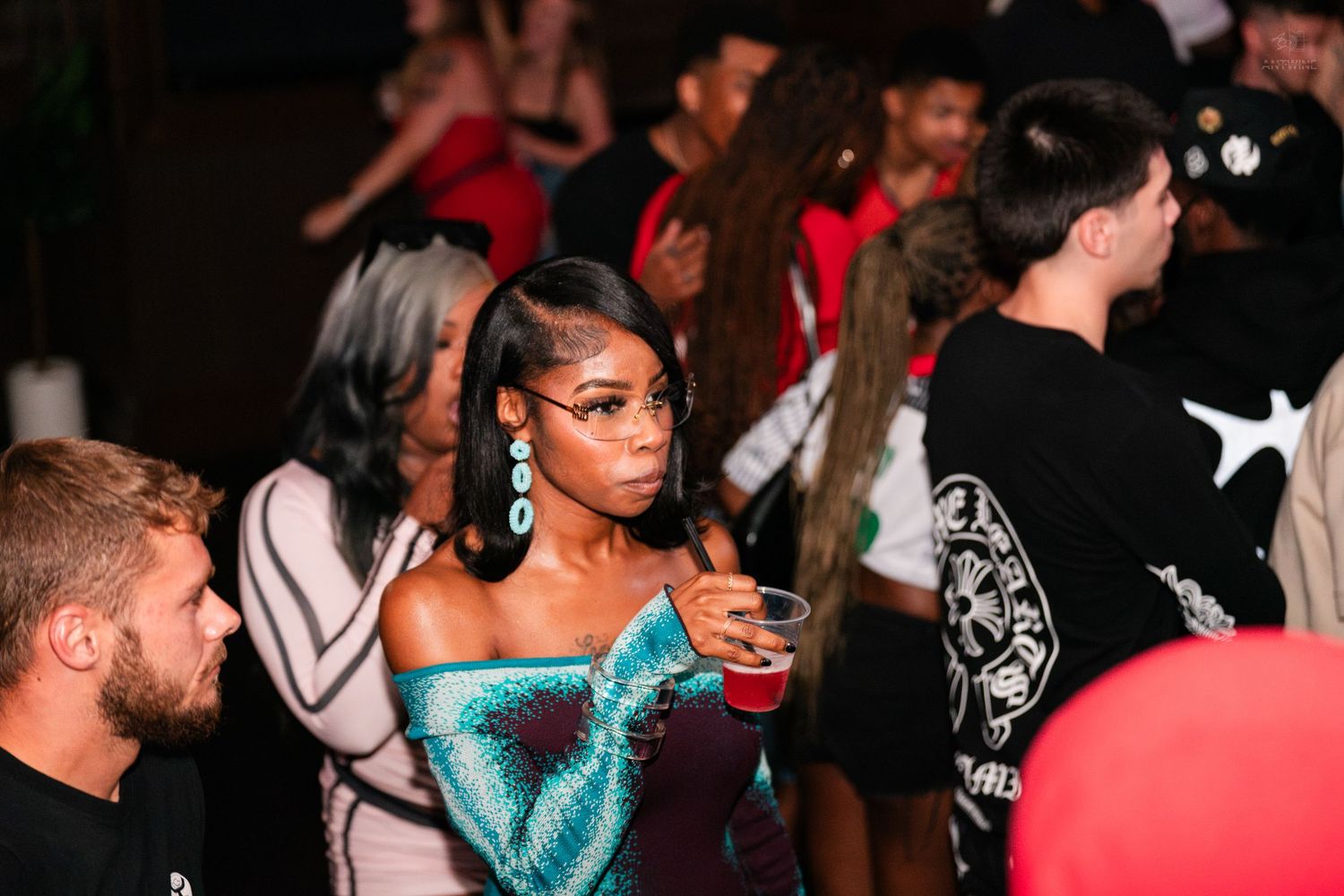 Stylish woman holding a red cup at a lively nightclub party event.