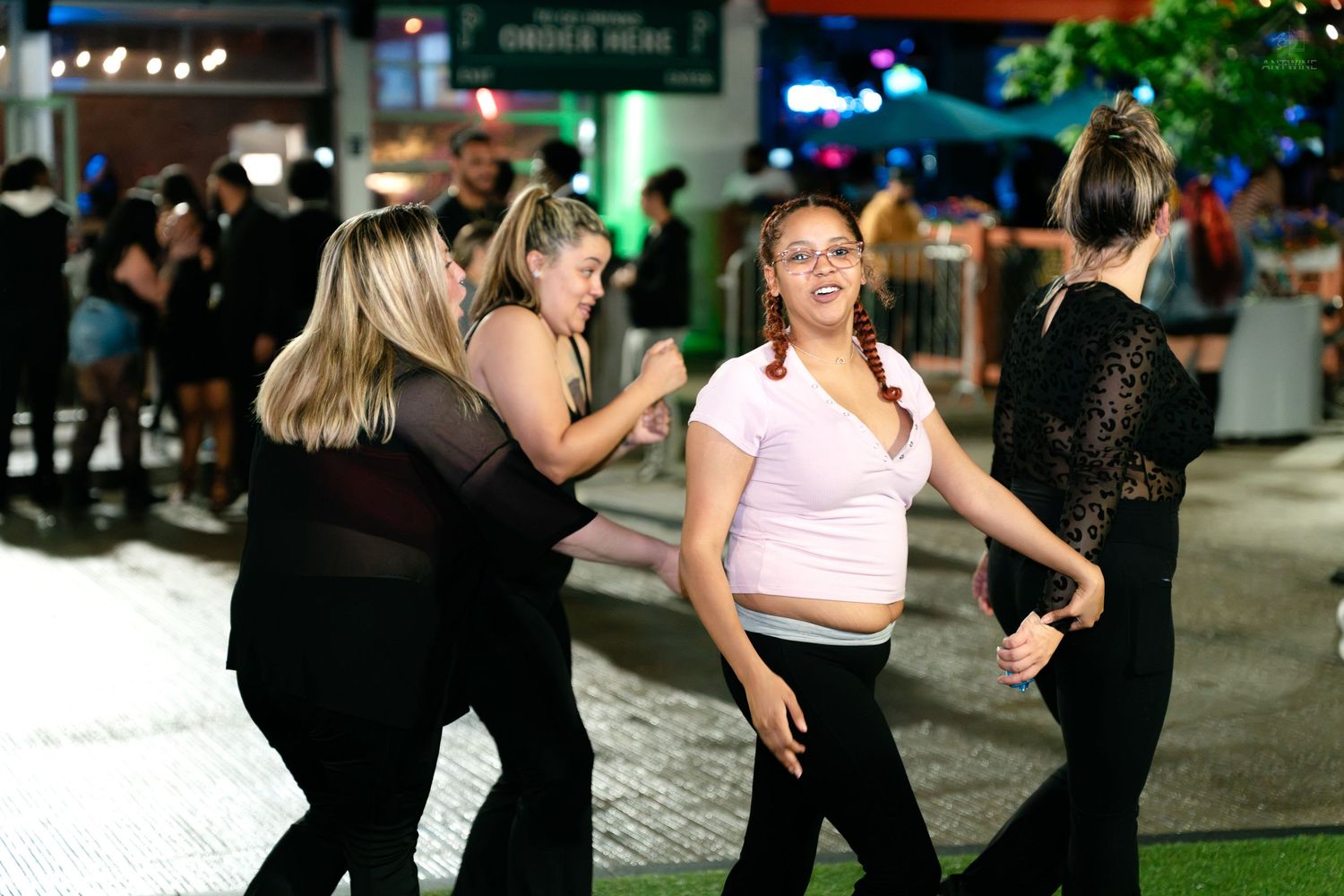 Group of women dancing and socializing at outdoor nighttime event on paved area.