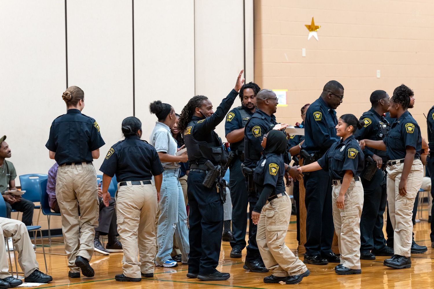 Police officers in dark uniforms engage with youth participants inside a school gymnasium at a community event.