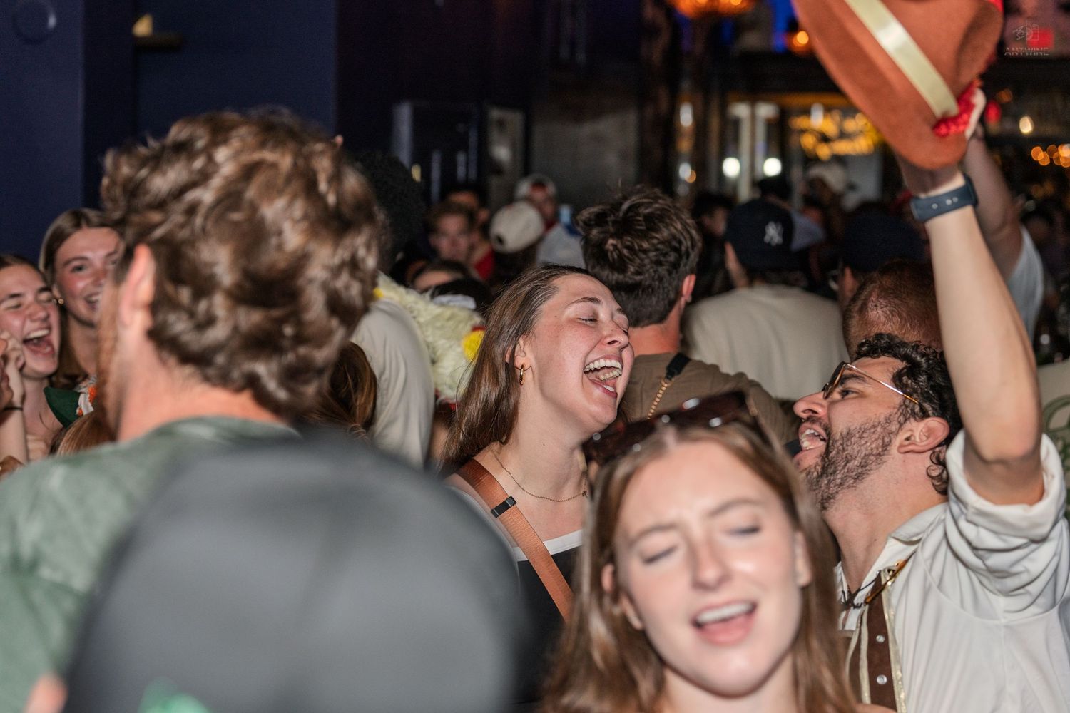 Crowd of young people laughing and celebrating at a lively indoor party event.