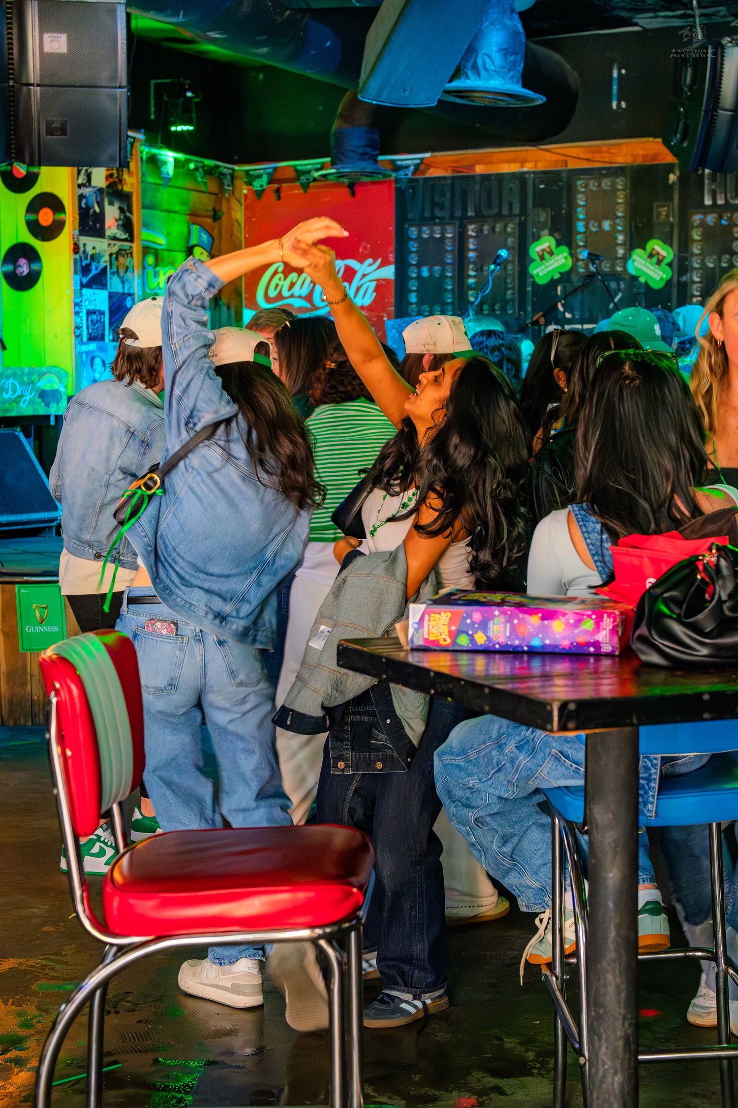 Group of friends dancing and socializing at a vibrant neon-lit bar with Coca-Cola signage.