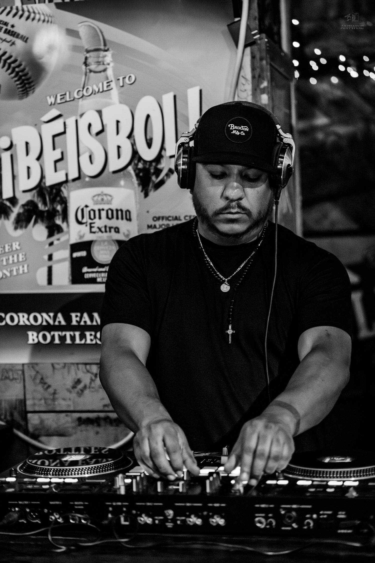 DJ wearing headphones and black cap mixing tracks at turntables in black and white photo.