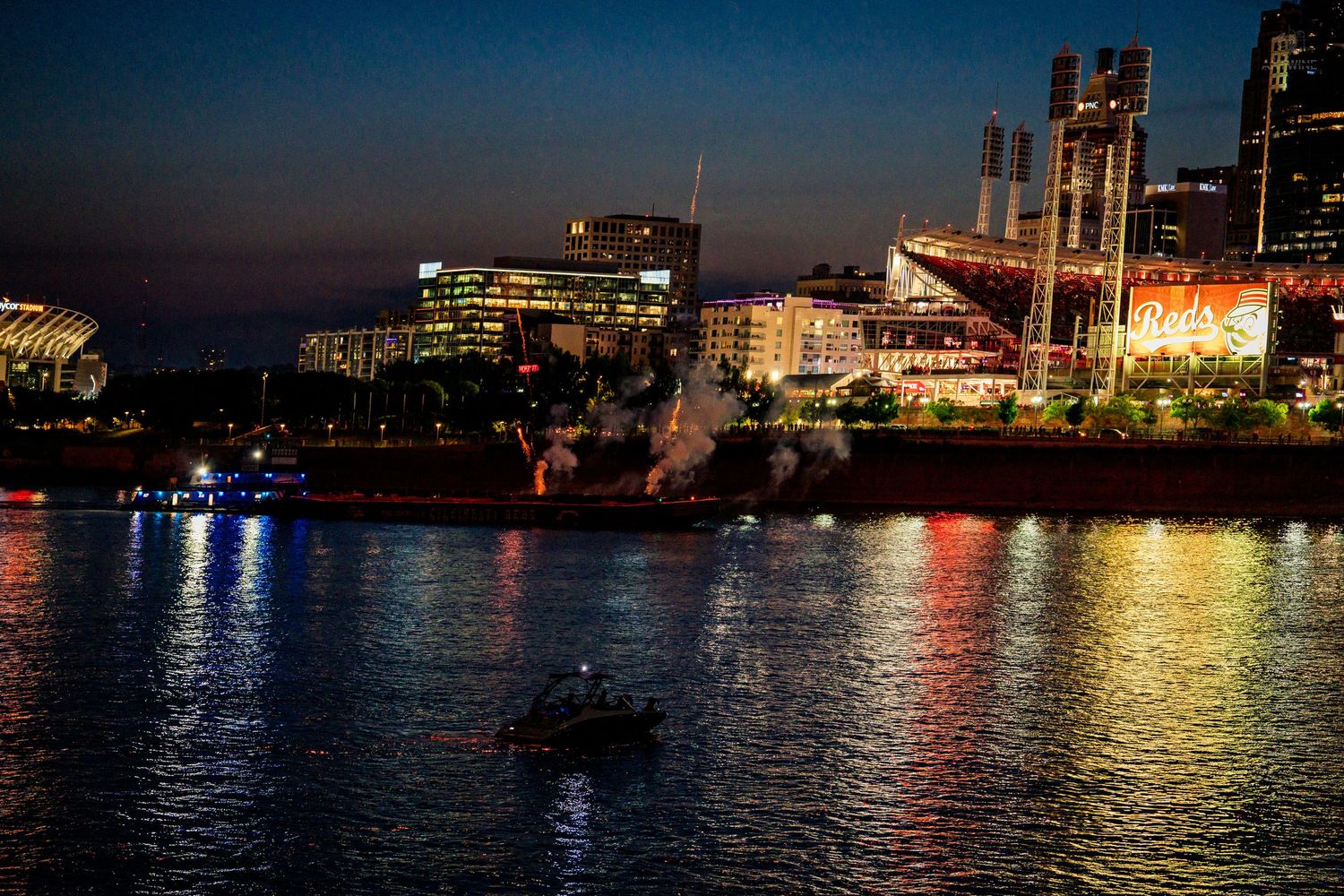 Cincinnati cityscape at night reflected on the Ohio River with a boat in the foreground.