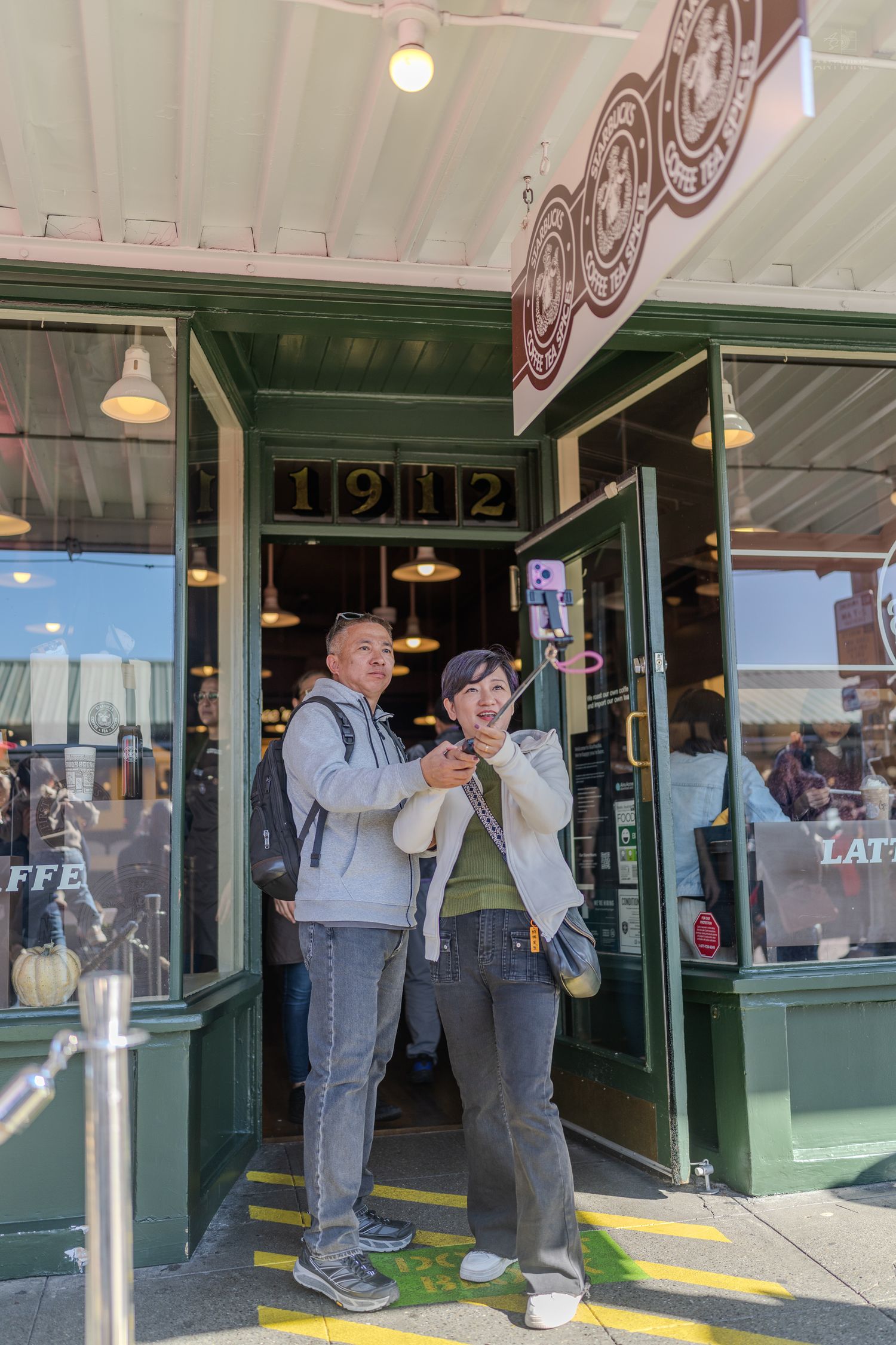 Two visitors taking a selfie outside the original 1912 Starbucks location at Pike Place Market in Seattle.