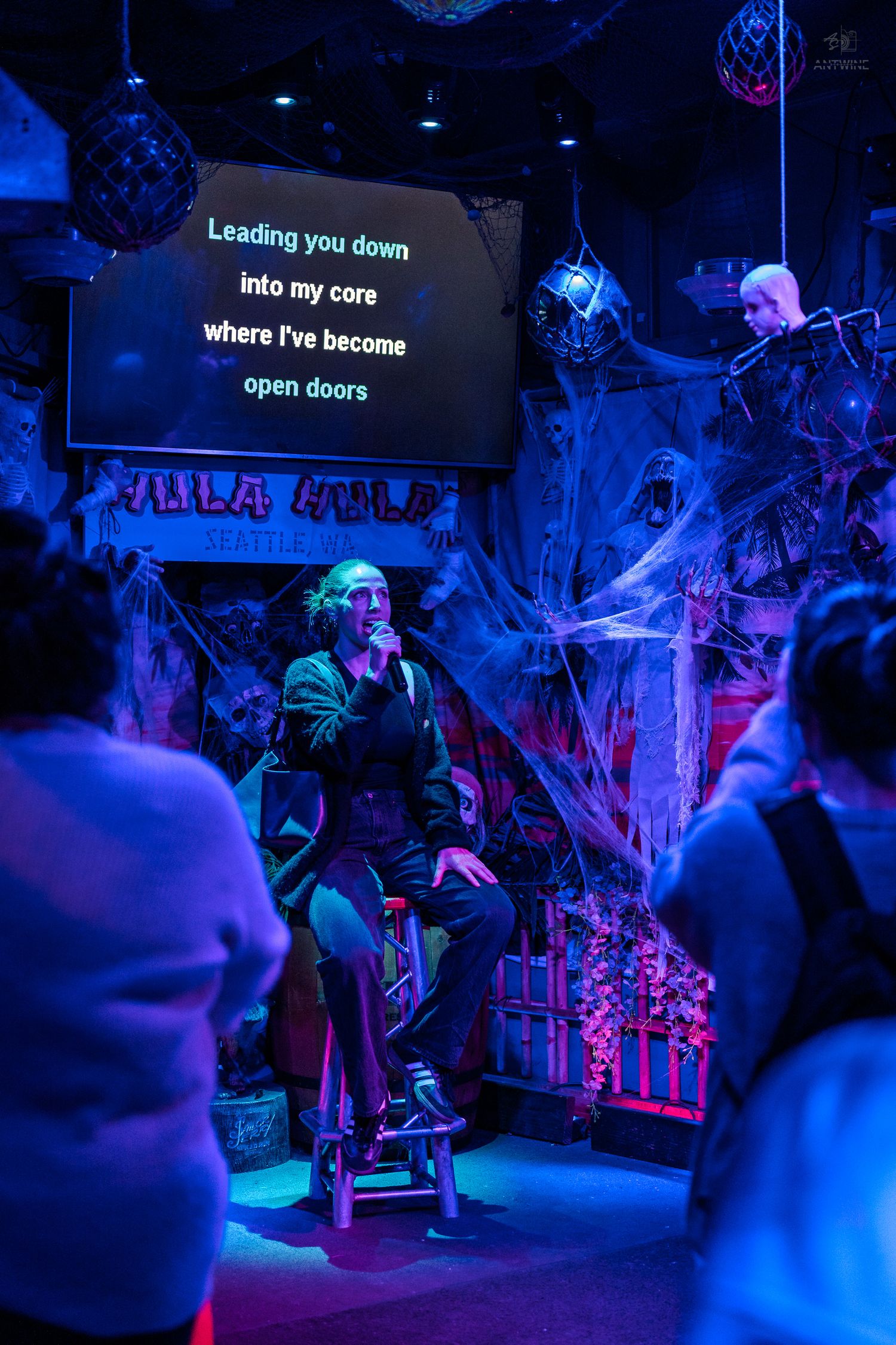 Performer singing karaoke on a Halloween-decorated stage with blue lighting and cobweb decor.
