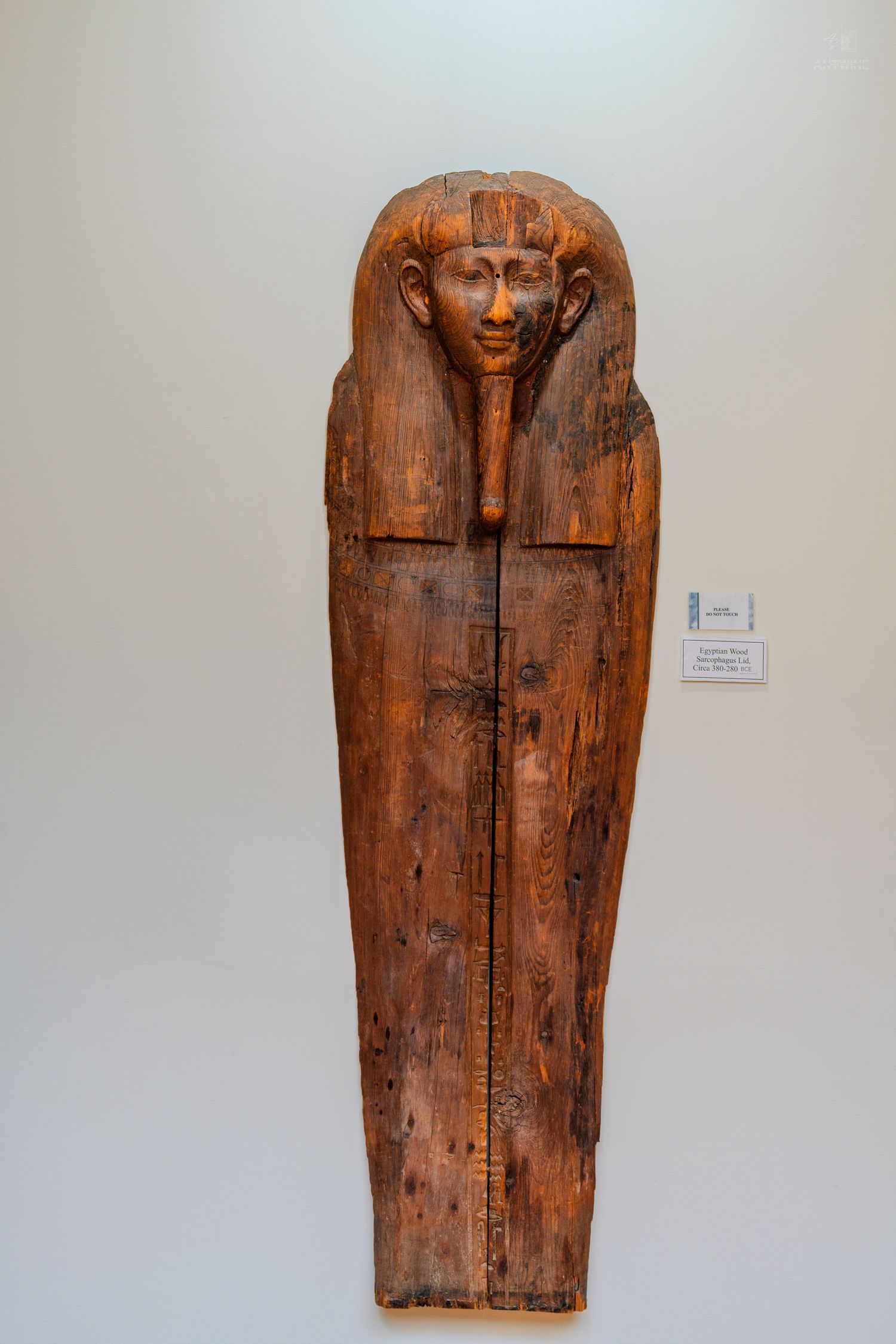 Ancient Egyptian wooden sarcophagus with carved pharaoh face displayed on museum wall.
