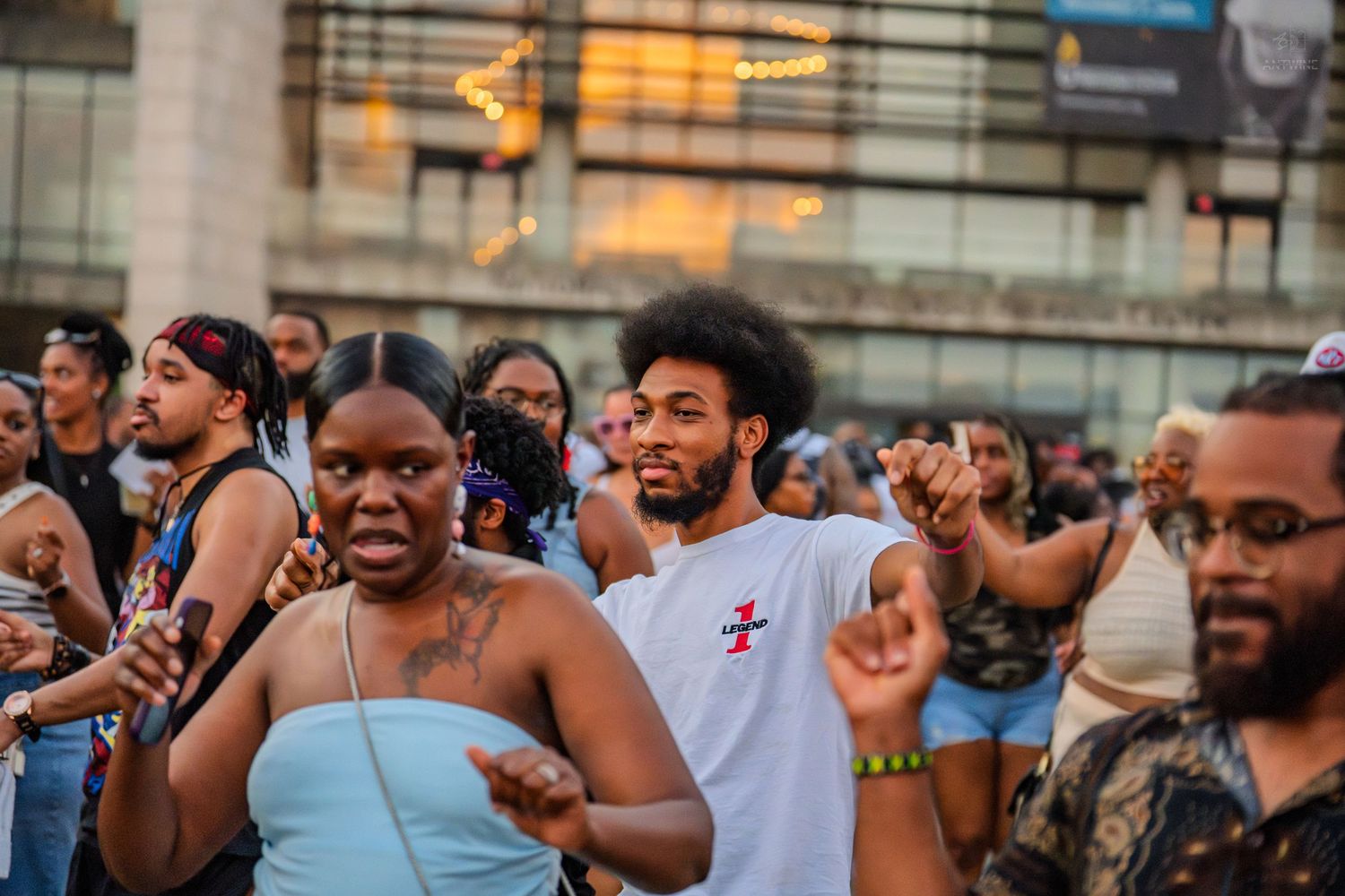 Diverse crowd of people dancing and celebrating at an outdoor urban music event at dusk.