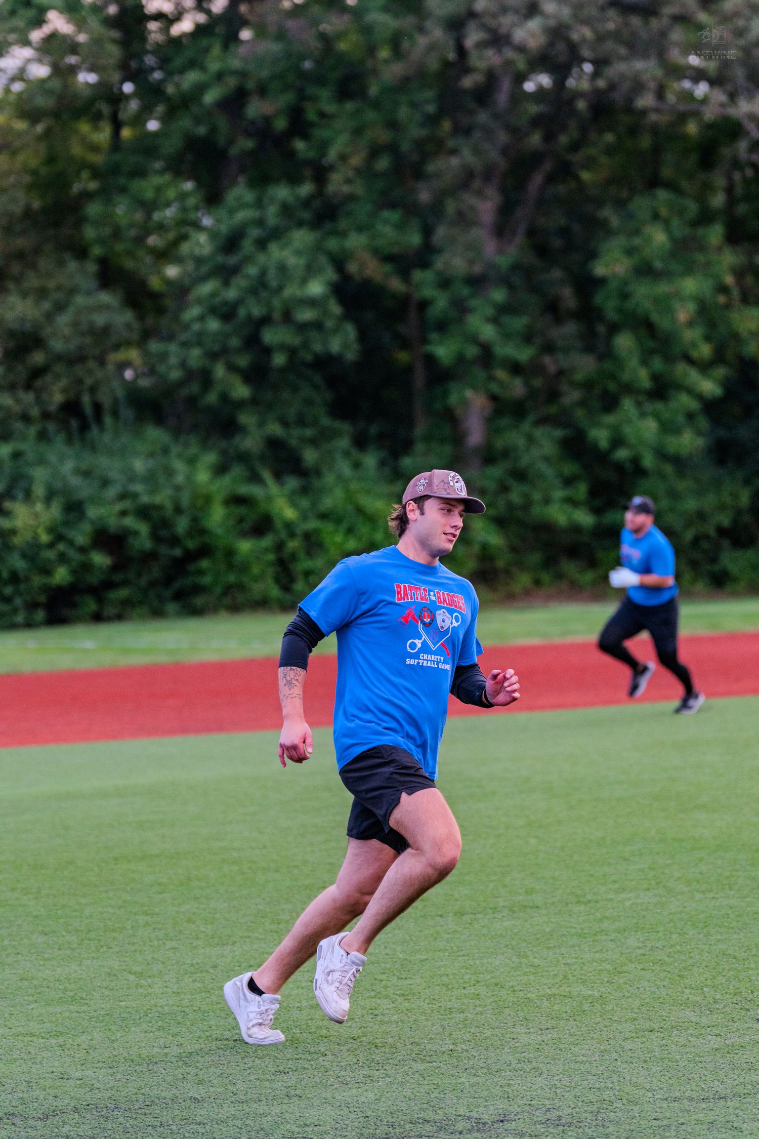 Young man in blue team shirt and cap running on green baseball field during outdoor game.