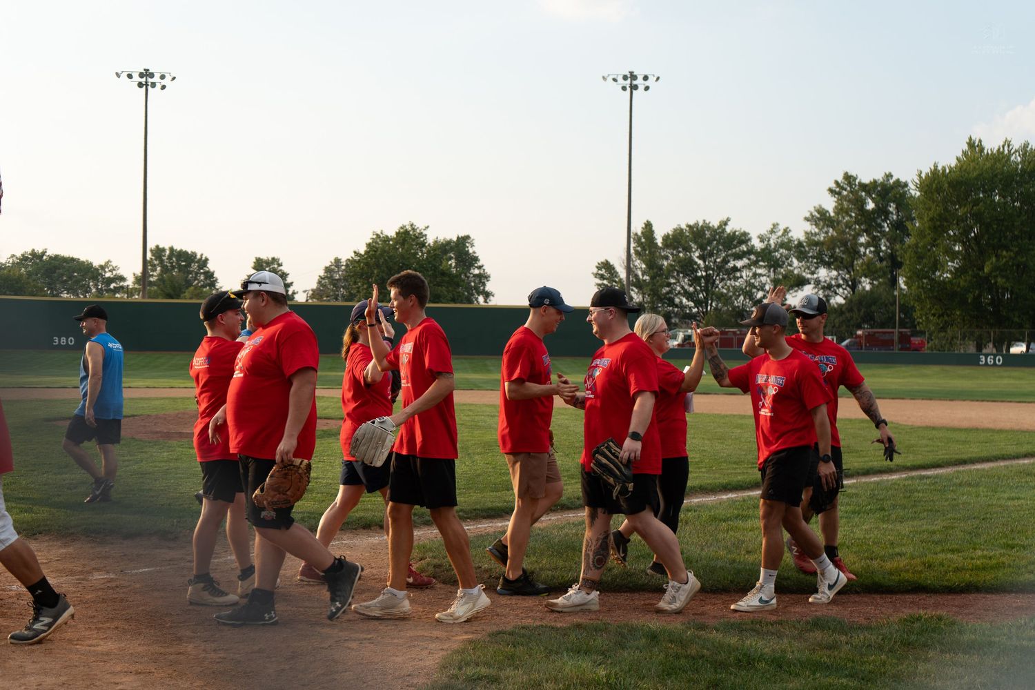 Team in red uniforms walks across baseball field during evening game.