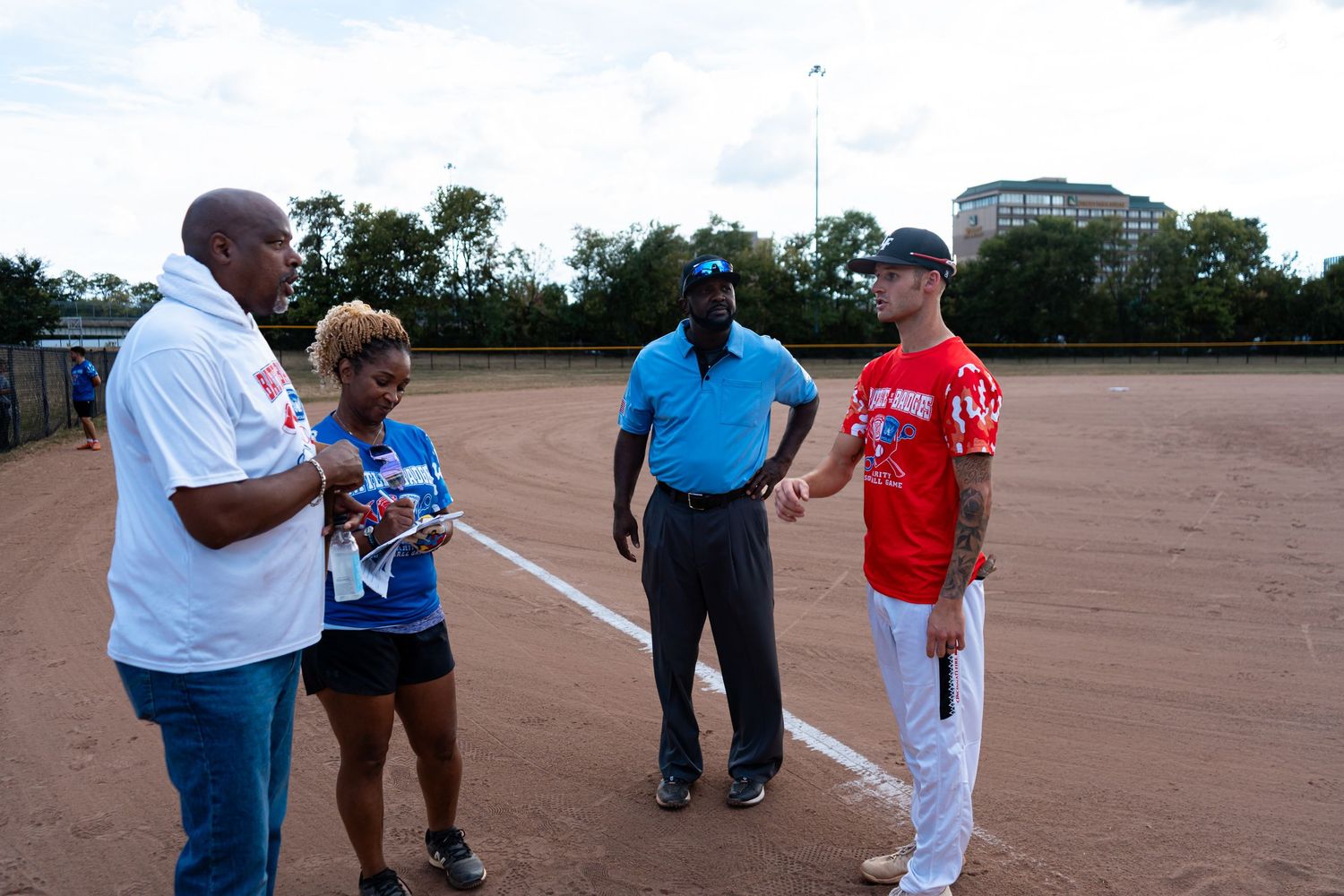 An umpire and players discuss rules on a softball field during an outdoor charity game event.