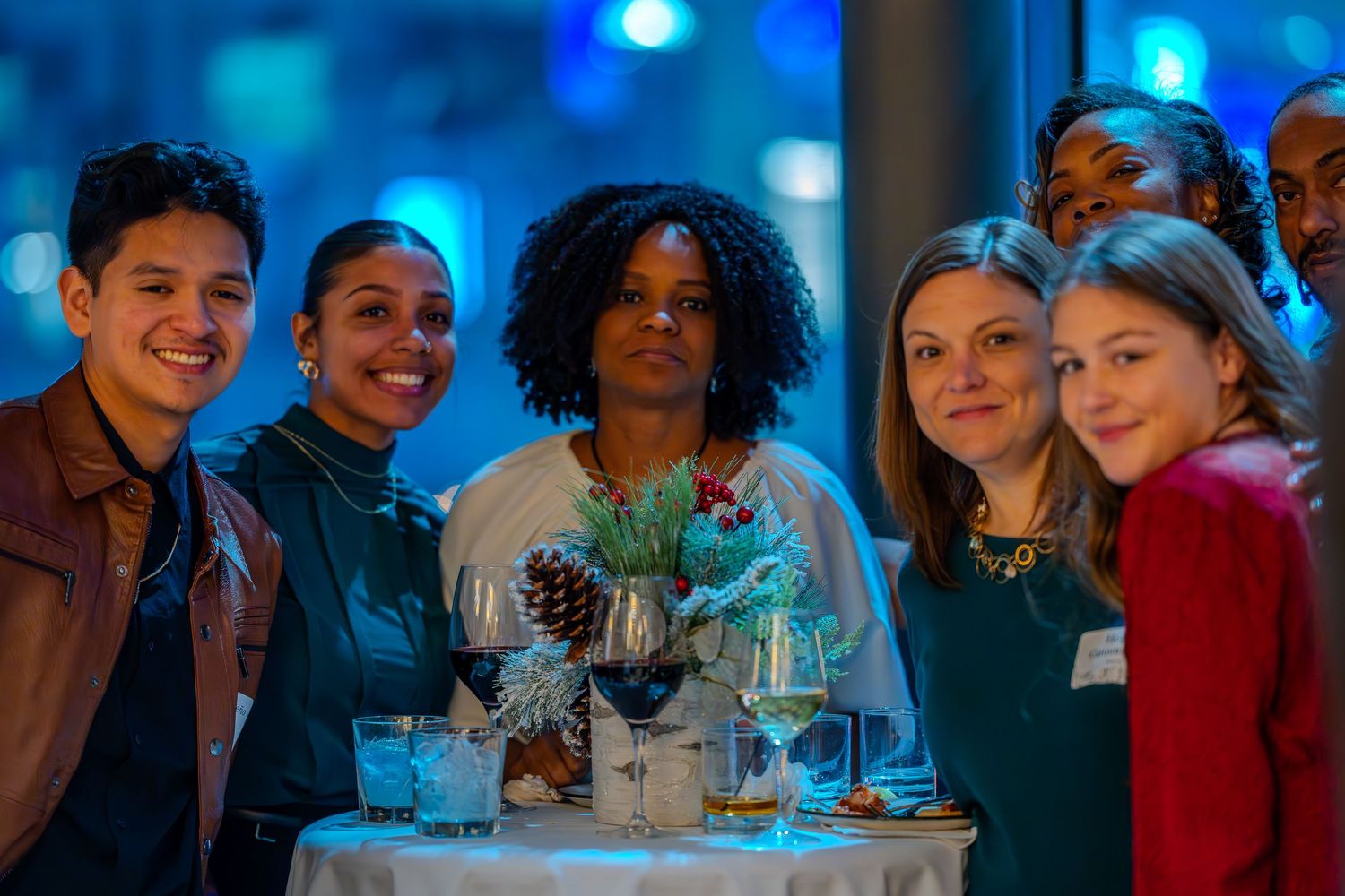 Diverse group of young adults smiling together at a festive holiday party around a decorated table.