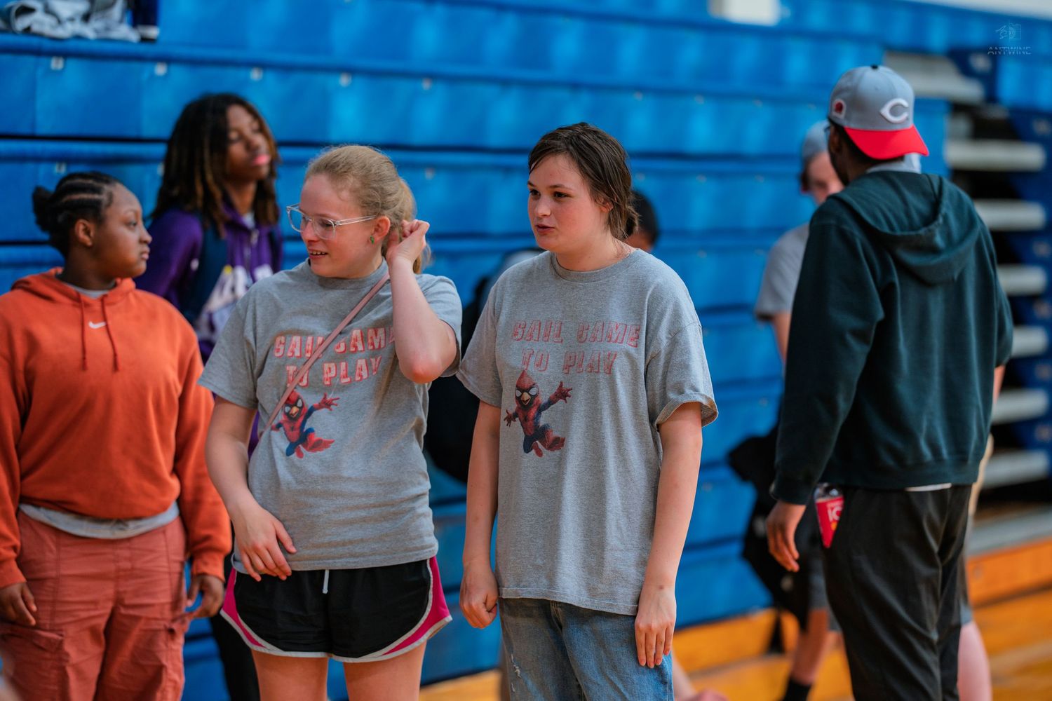 Students in matching gray shirts stand together in a school gymnasium during an indoor activity or sports event.