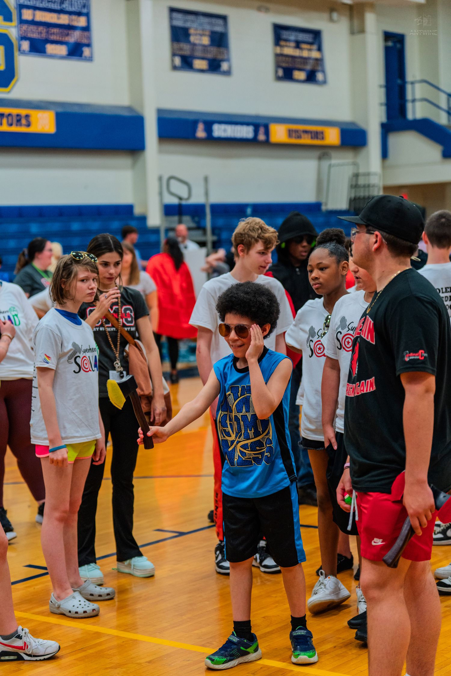 Children and teens participate in a Special Olympics basketball event inside a school gymnasium with blue and gold decor.