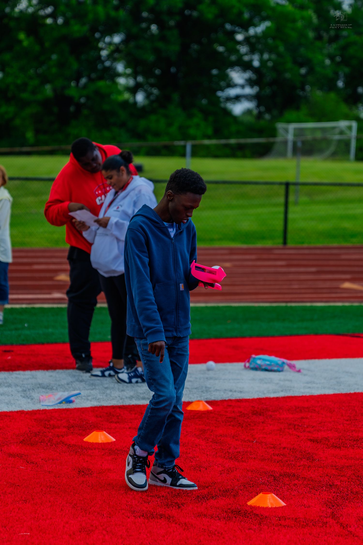 Young student walking on red turf field with orange cones during outdoor track and field activity event.