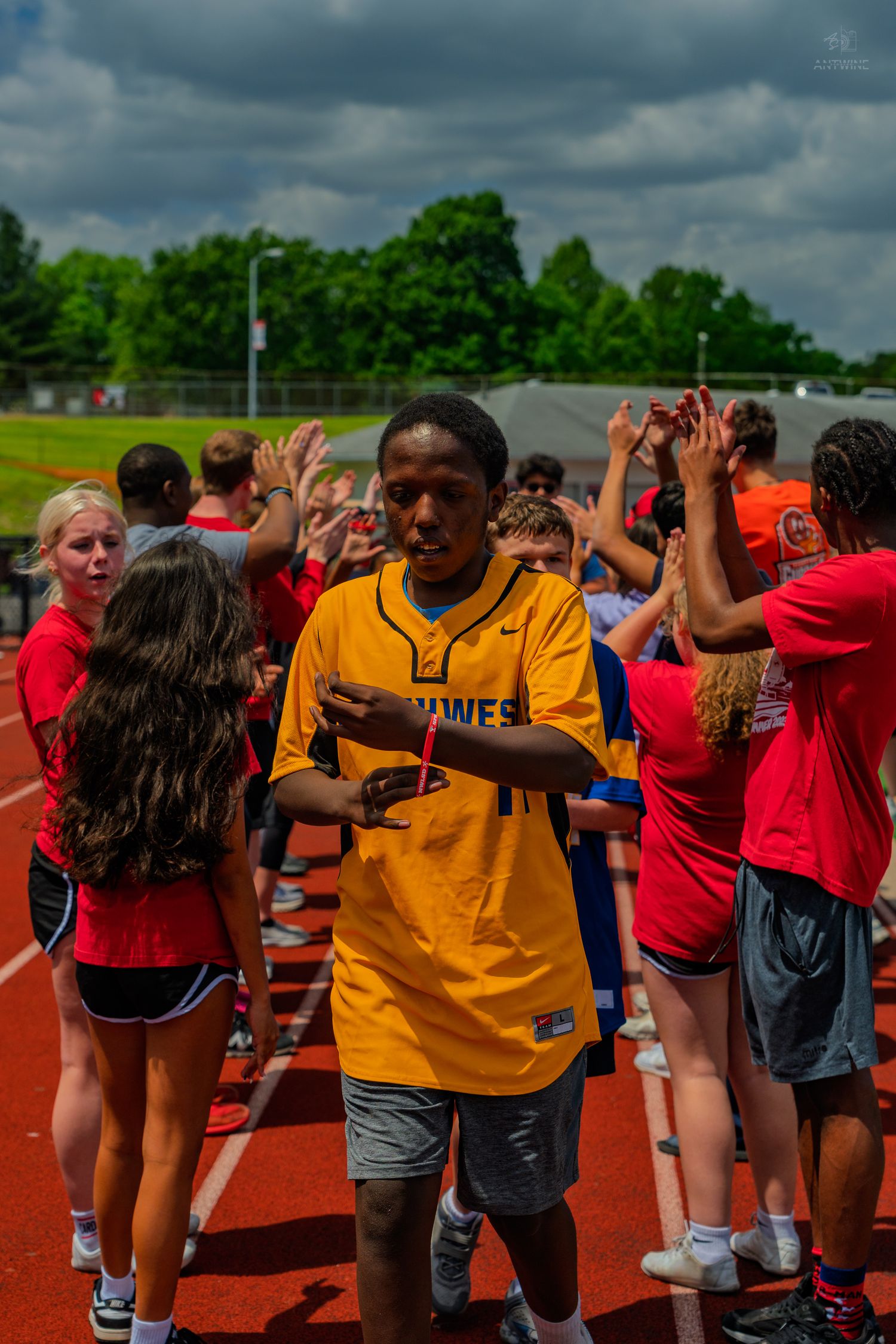 Student in gold jersey walks through congratulatory high-five line on red track during outdoor sports event.